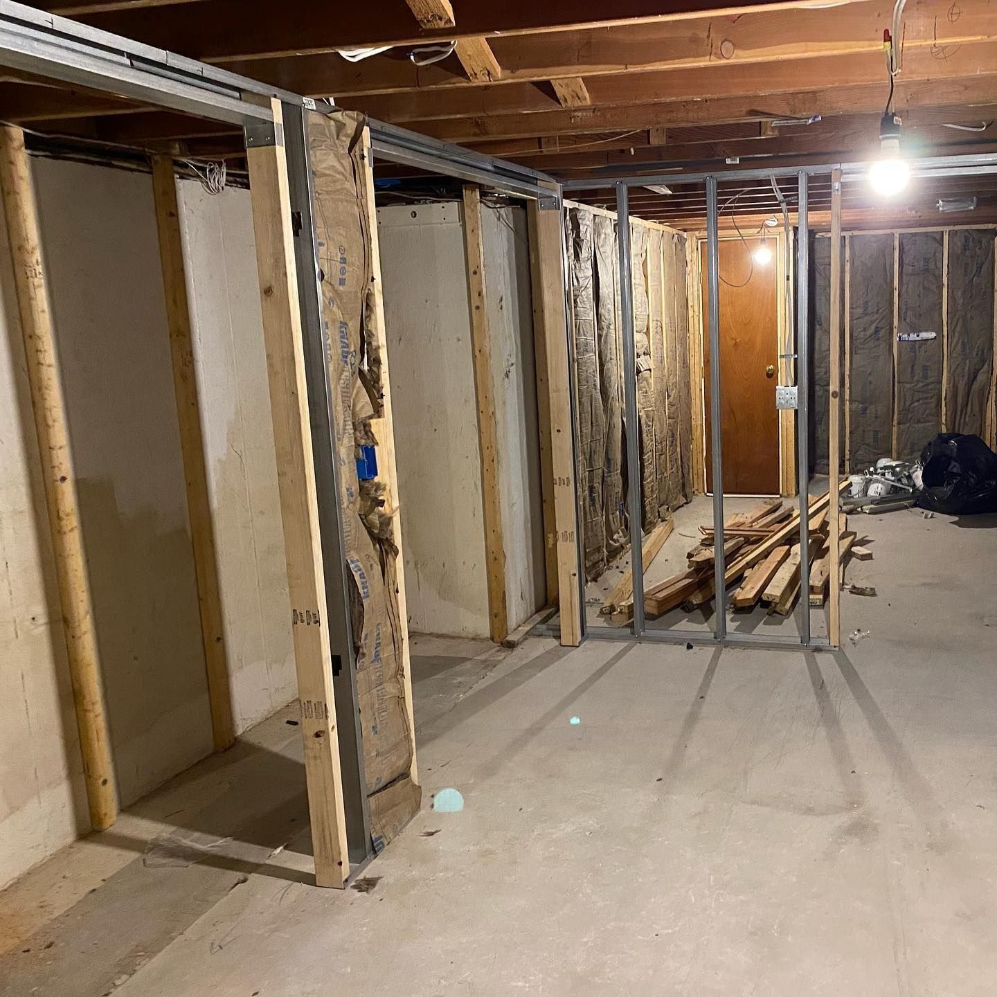 Basement under construction: framed walls, concrete floor, exposed insulation, wood, and metal studs.