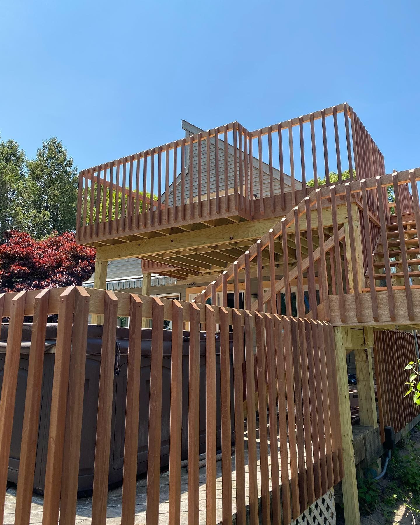 Wooden deck with railings, stairs, and a hot tub on a sunny day.
