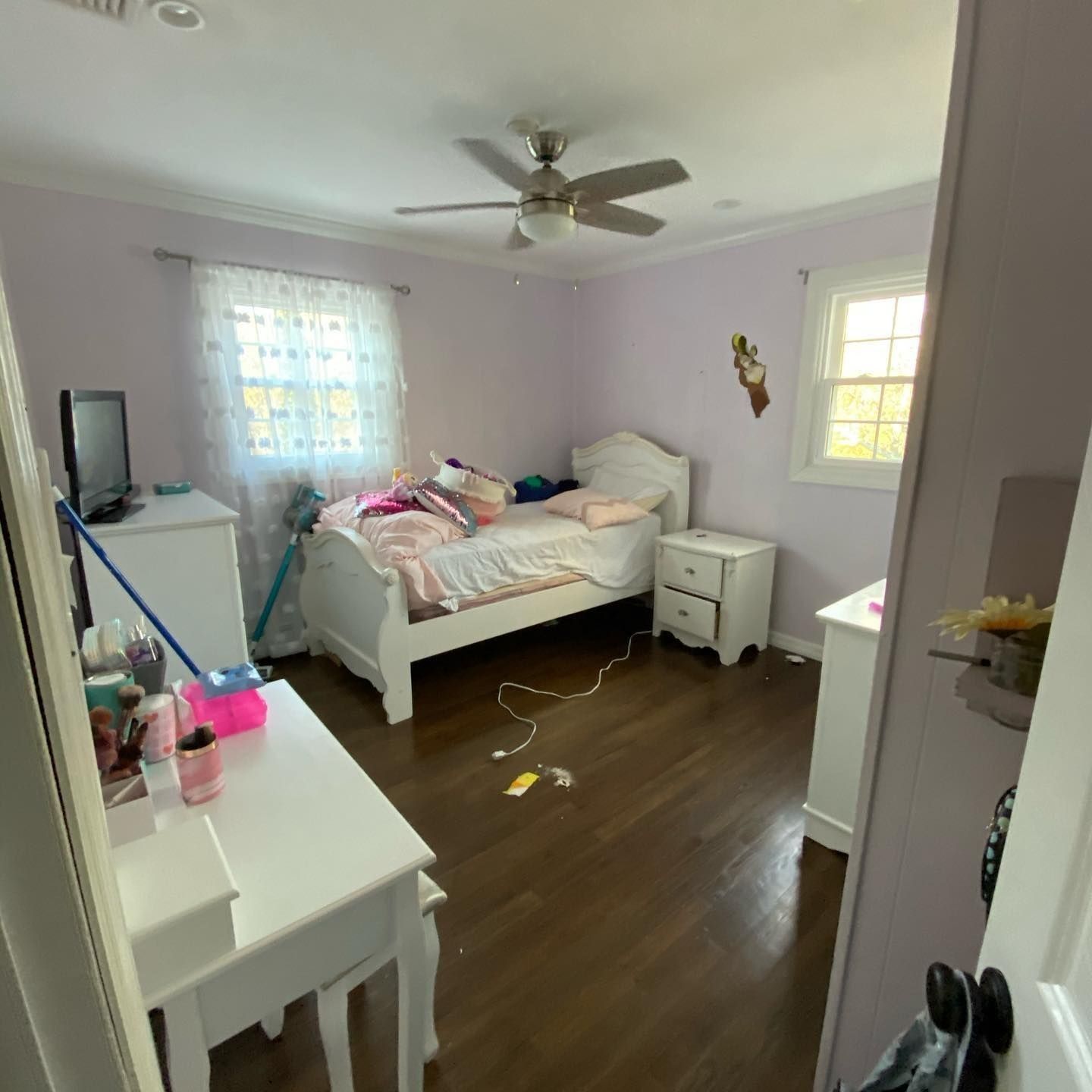 Bedroom with pink walls, a white bed, and furniture. Dark wood floors.