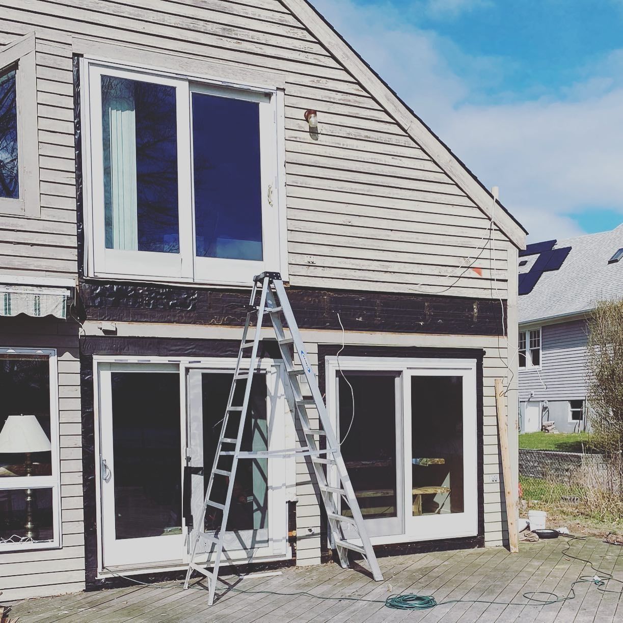 Exterior of a building with a ladder leaning against it. Two sliding glass doors and a large window are visible.