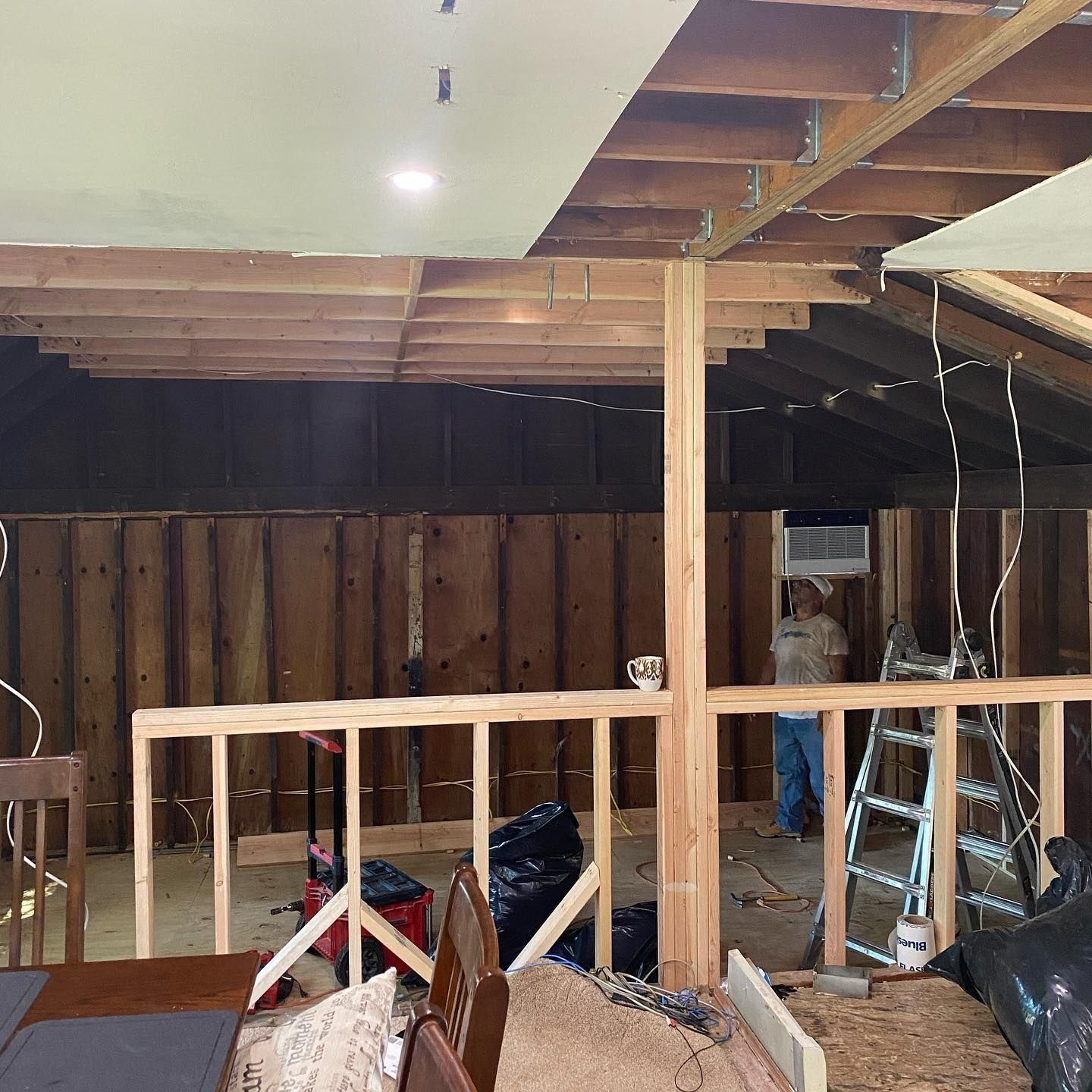 Interior construction site with exposed wood framing and a person standing by an air conditioning unit.