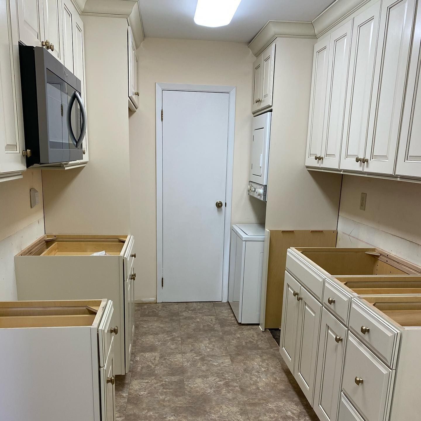 Kitchen with off-white cabinets, microwave, washing machine, and bare cabinet frames; ready for renovations.