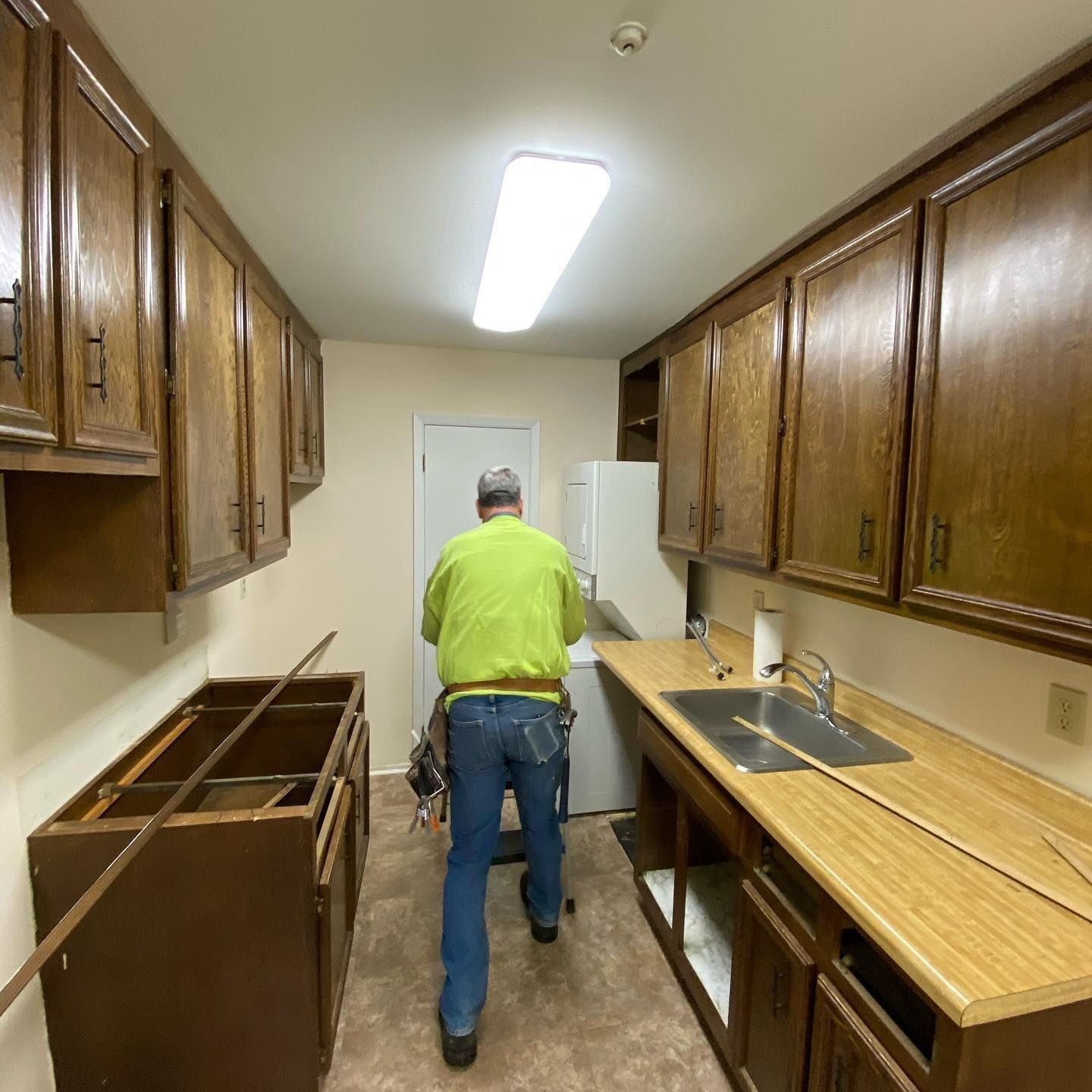 A person works in a room with wood cabinets, a sink, and a washing machine.