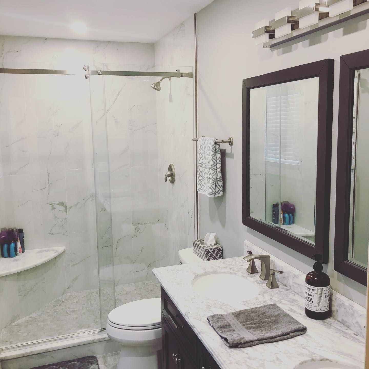 Bathroom with marble-look shower and countertop, dark wood mirror frames, and dark cabinet.