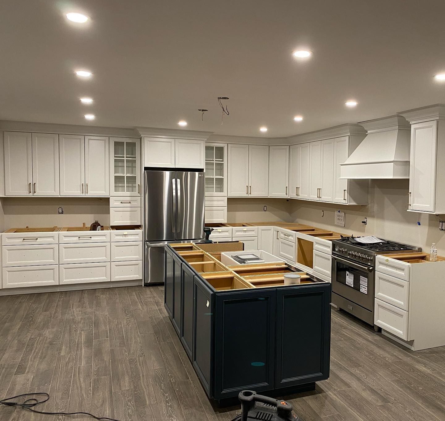 White kitchen with dark blue island under construction. Stainless steel fridge and gas range.
