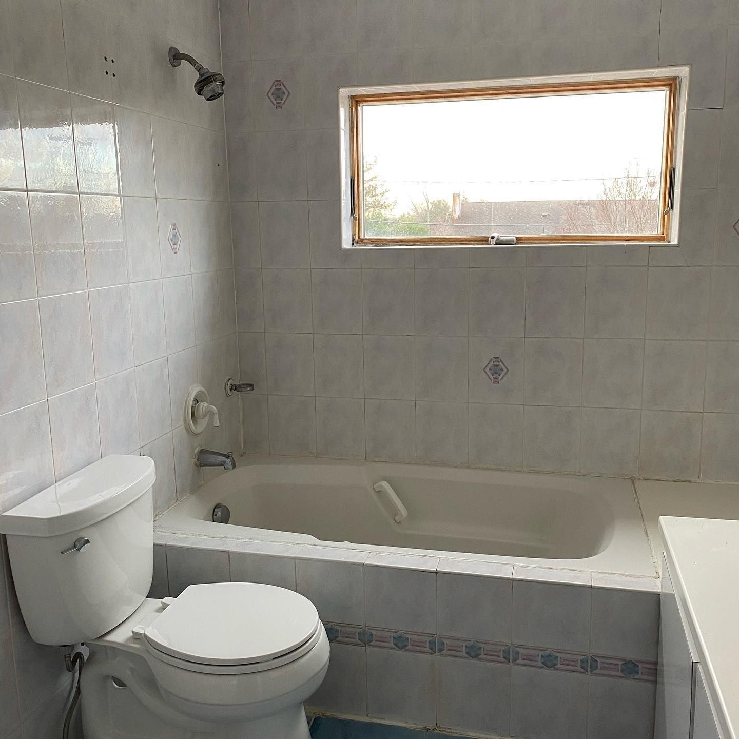Bathroom with a white toilet, tub, and tiled walls. A small window lets in light.
