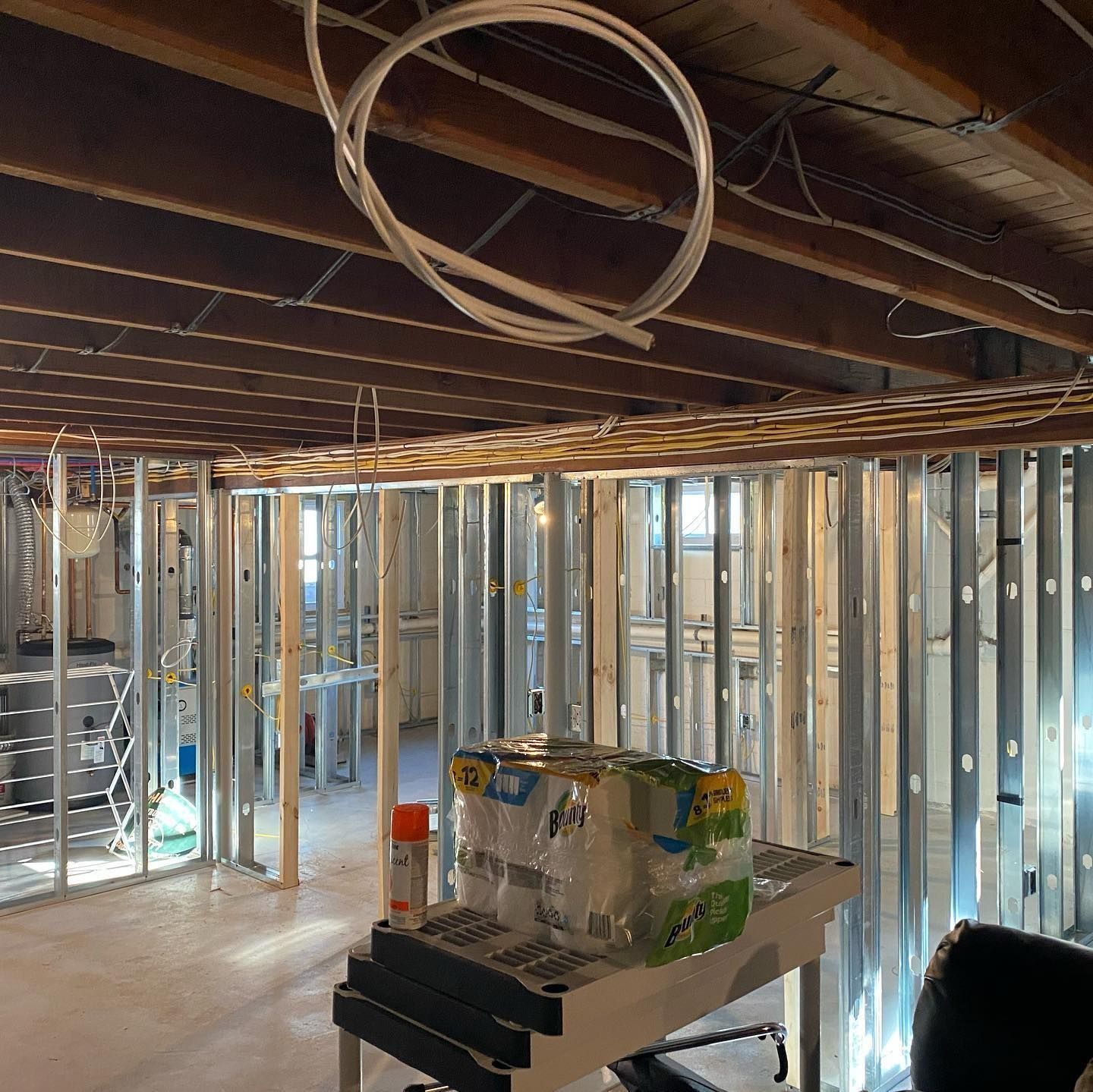 Interior of a room under construction, with metal studs and exposed ceiling joists. A stack of water bottles sits on a table.