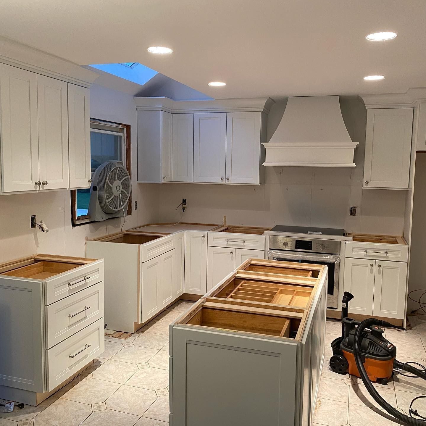 Kitchen remodel: white cabinets, island, range, and hood under construction with tools.