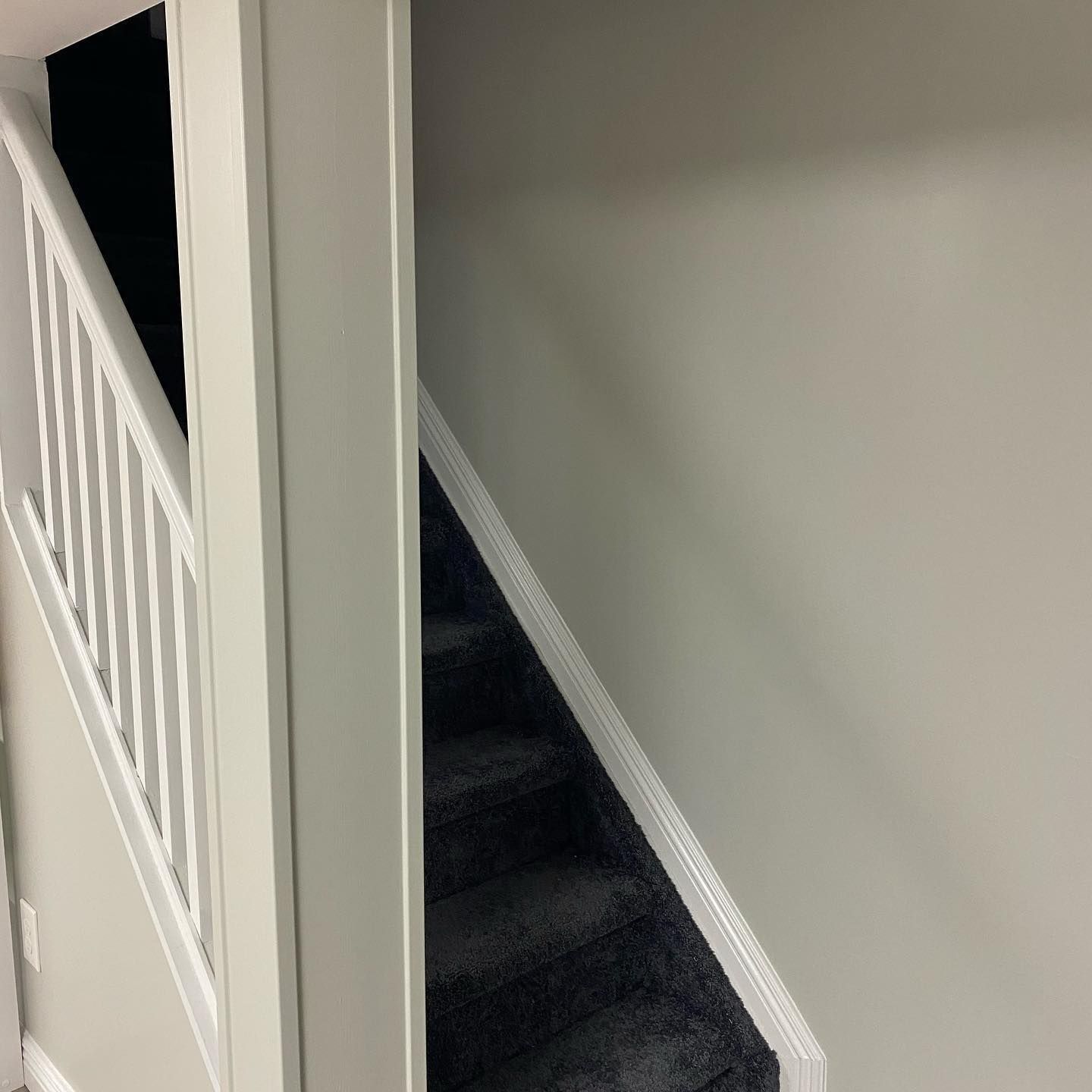 Staircase with white railing on the left and gray carpeted steps, against a light gray wall.