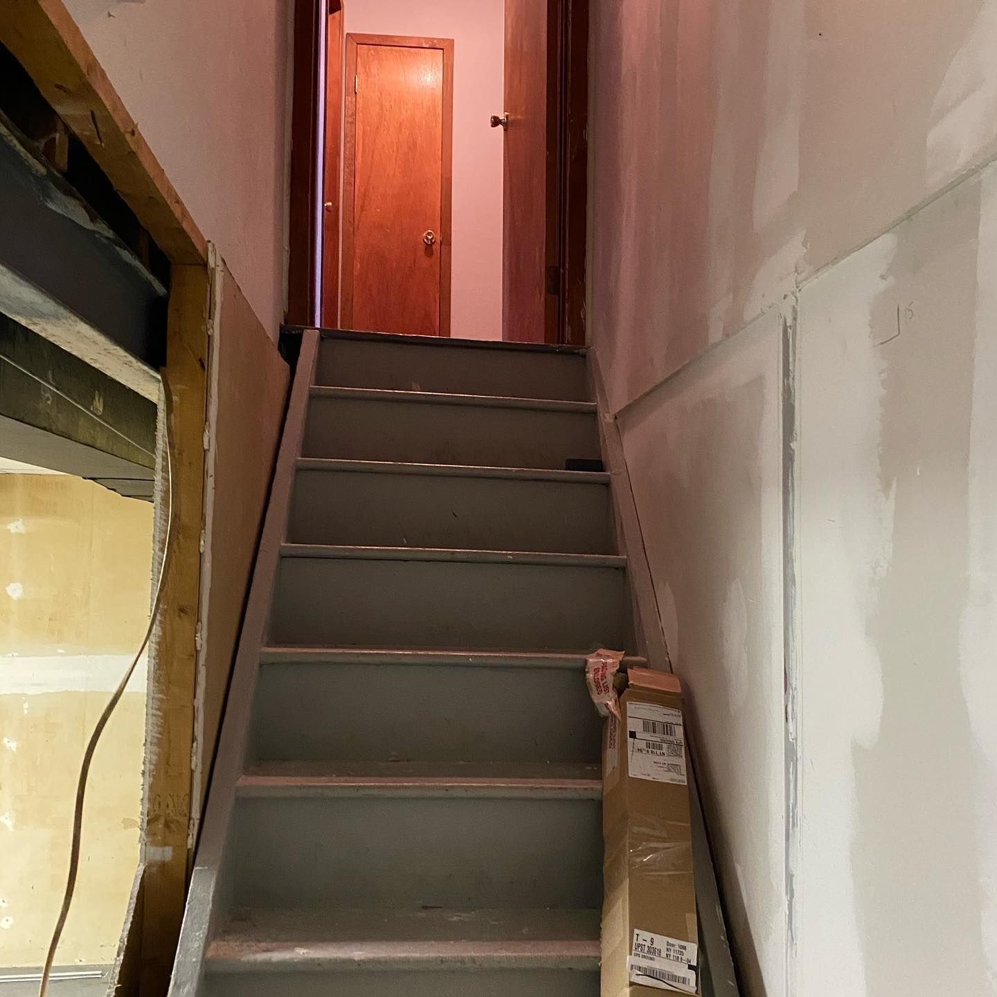 Staircase leading up to a doorway. Walls are partially finished. Box on bottom step.