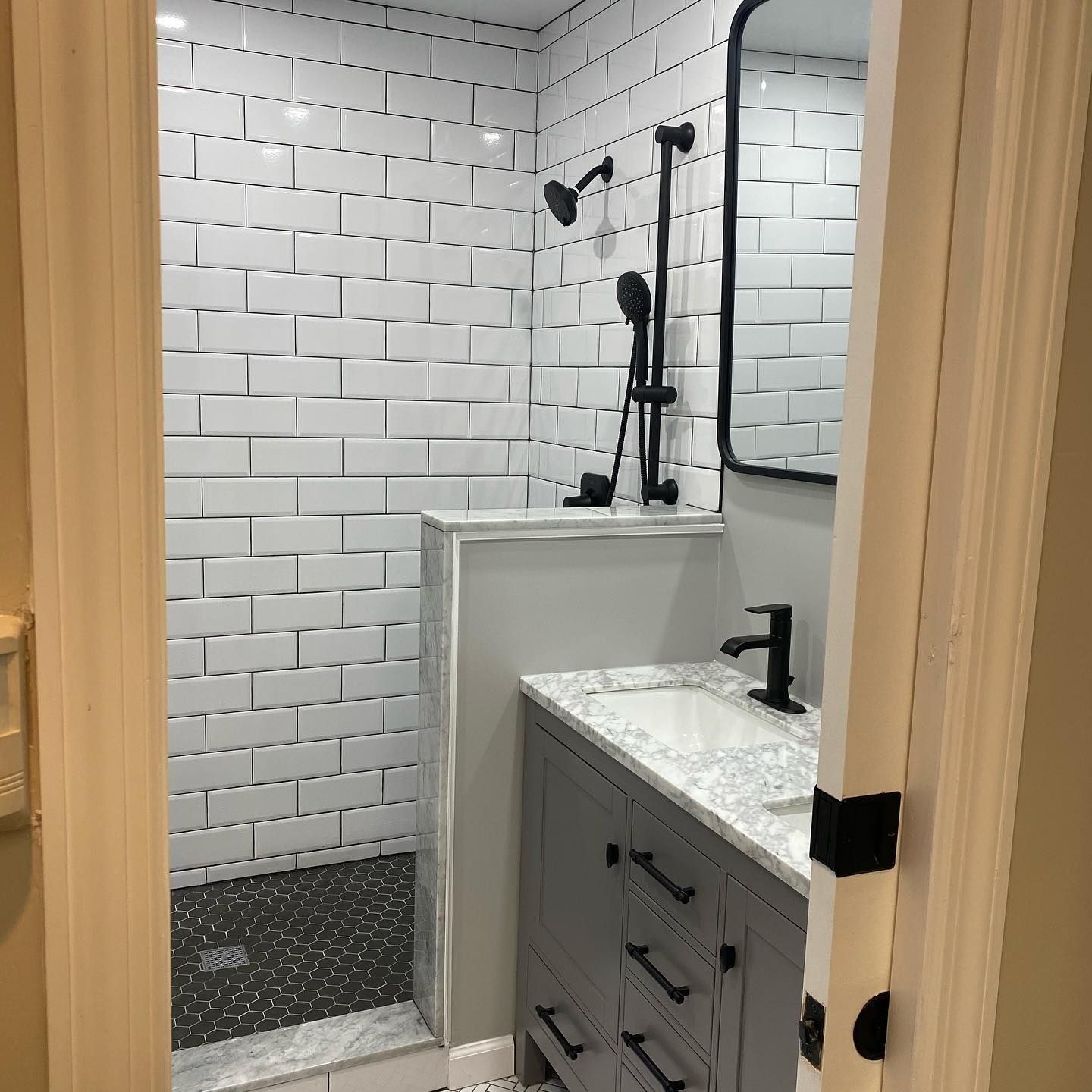 Bathroom with white subway tile shower, gray vanity, and black fixtures.