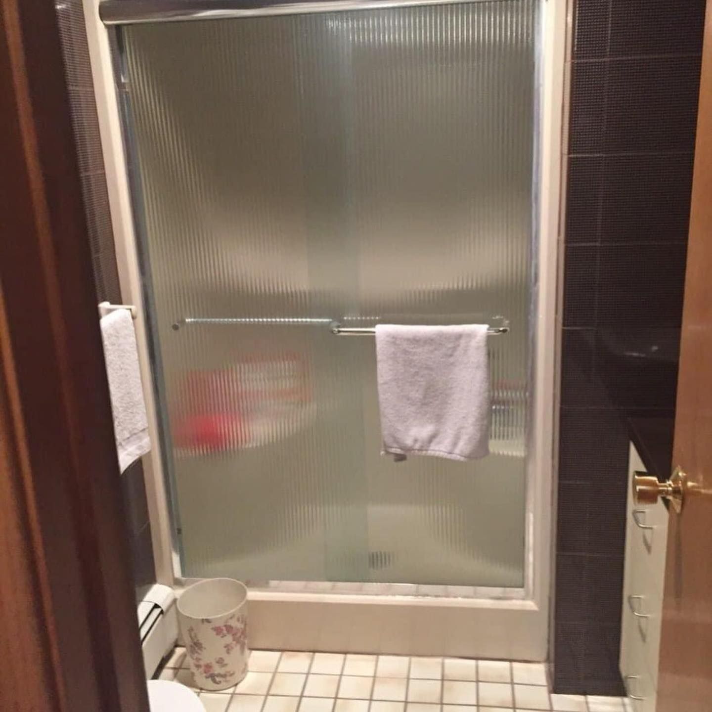 Shower with sliding glass doors, a towel rack, and a white towel hanging on the door.