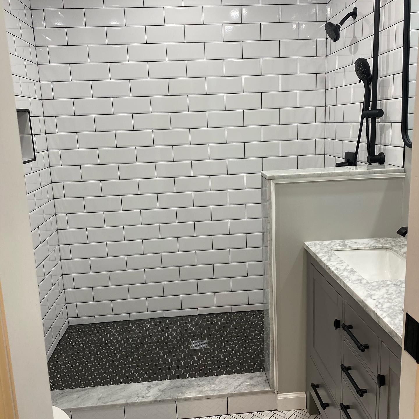 Bathroom with white subway tile shower, black fixtures, gray vanity, and dark pebble floor.