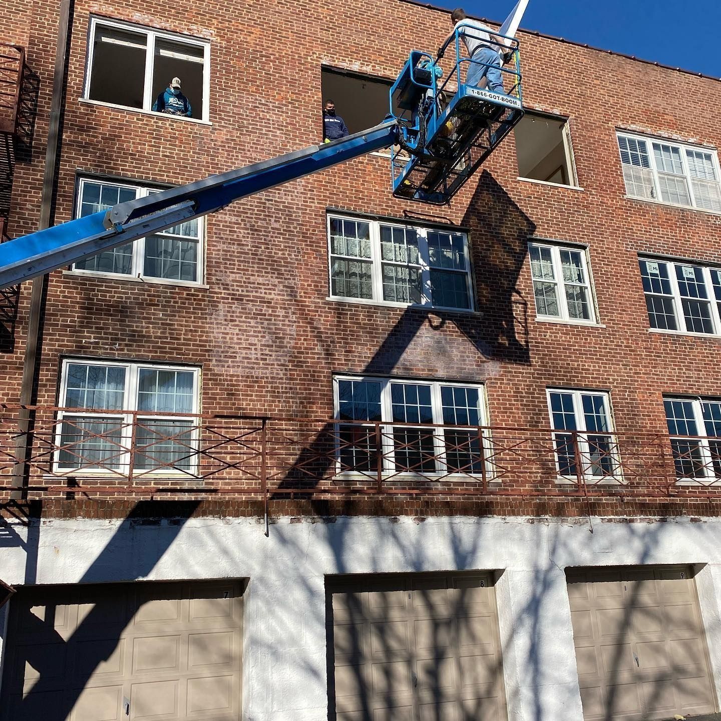 Workers on a lift replacing windows of a brick building.