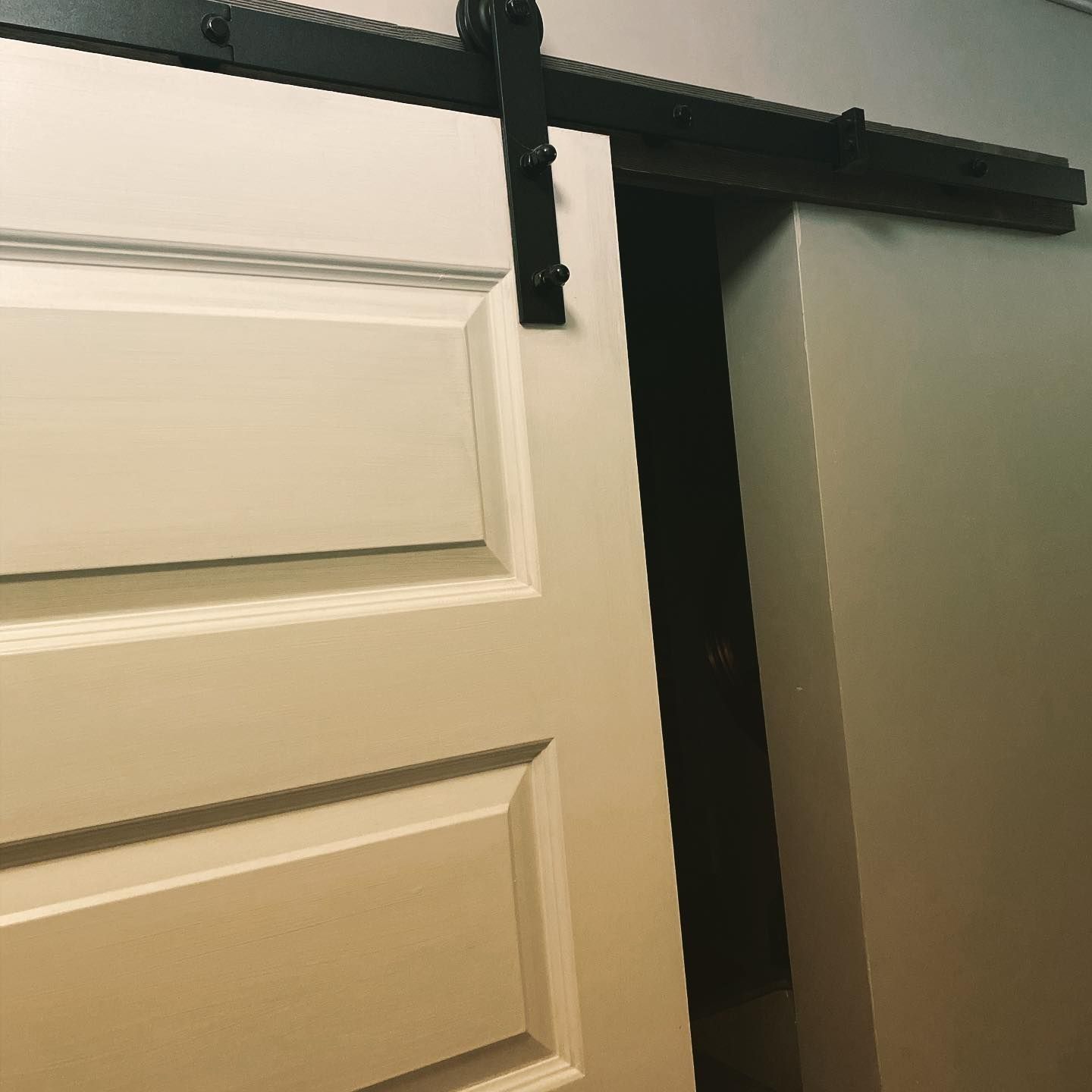 White interior door partially open, black sliding hardware on top.