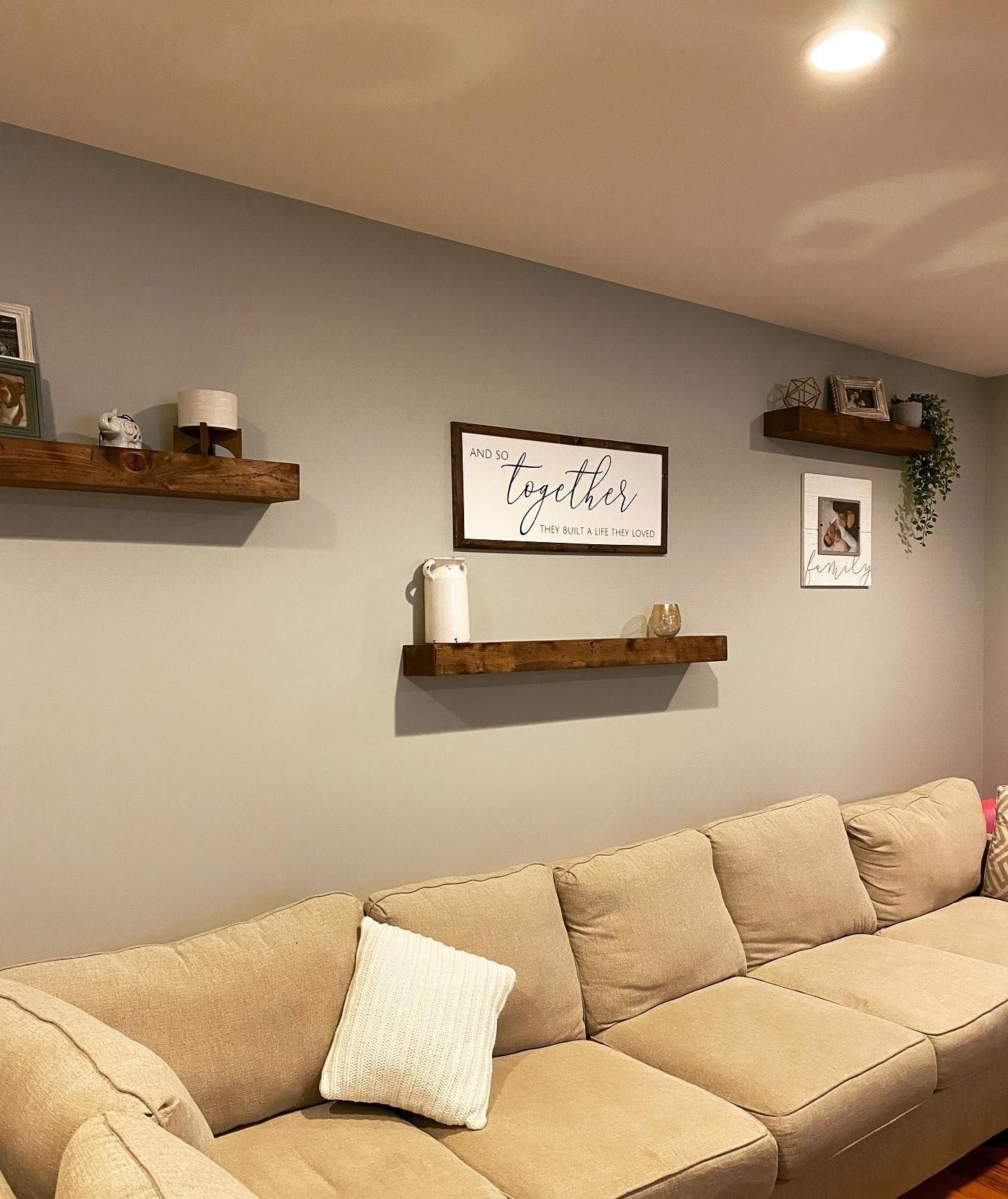 Gray living room with a beige couch and wooden floating shelves. 