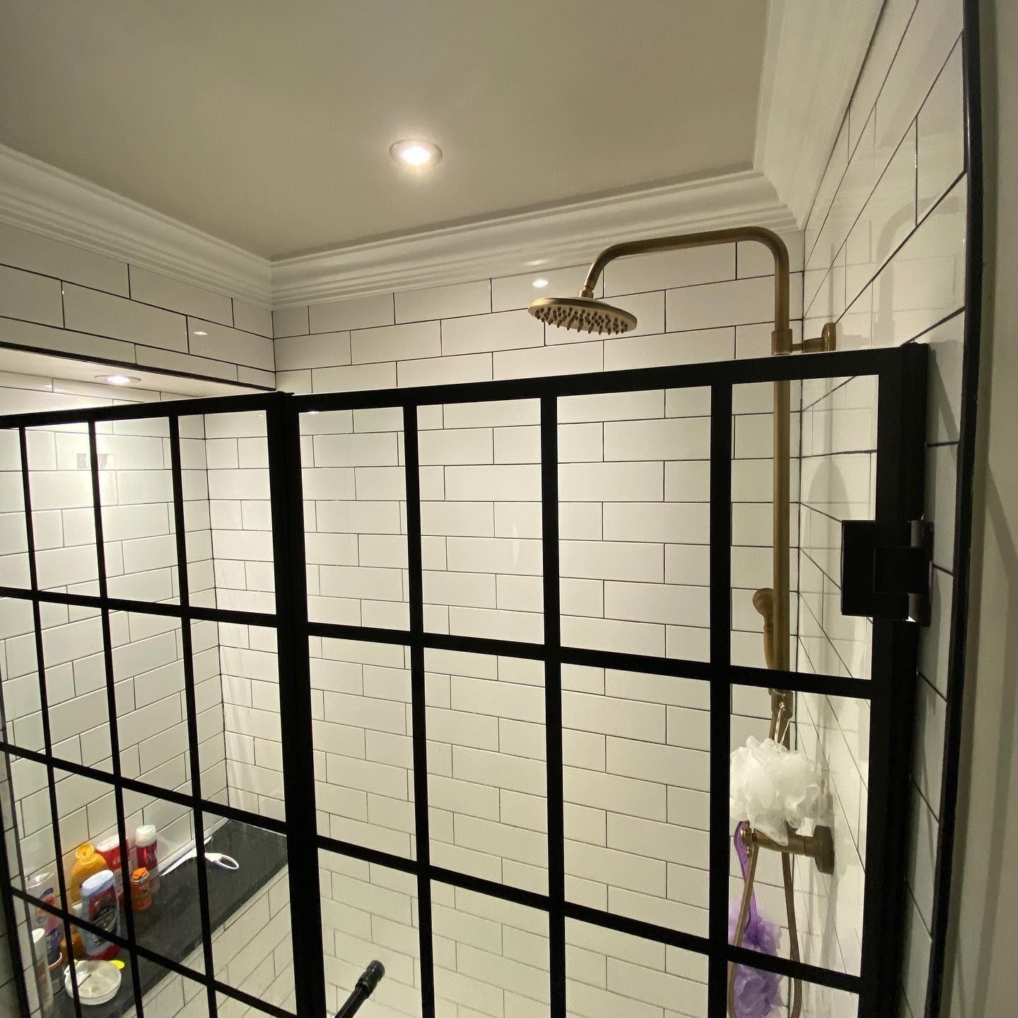 Black-framed shower enclosure with white subway tile walls, brass showerhead and fixtures.