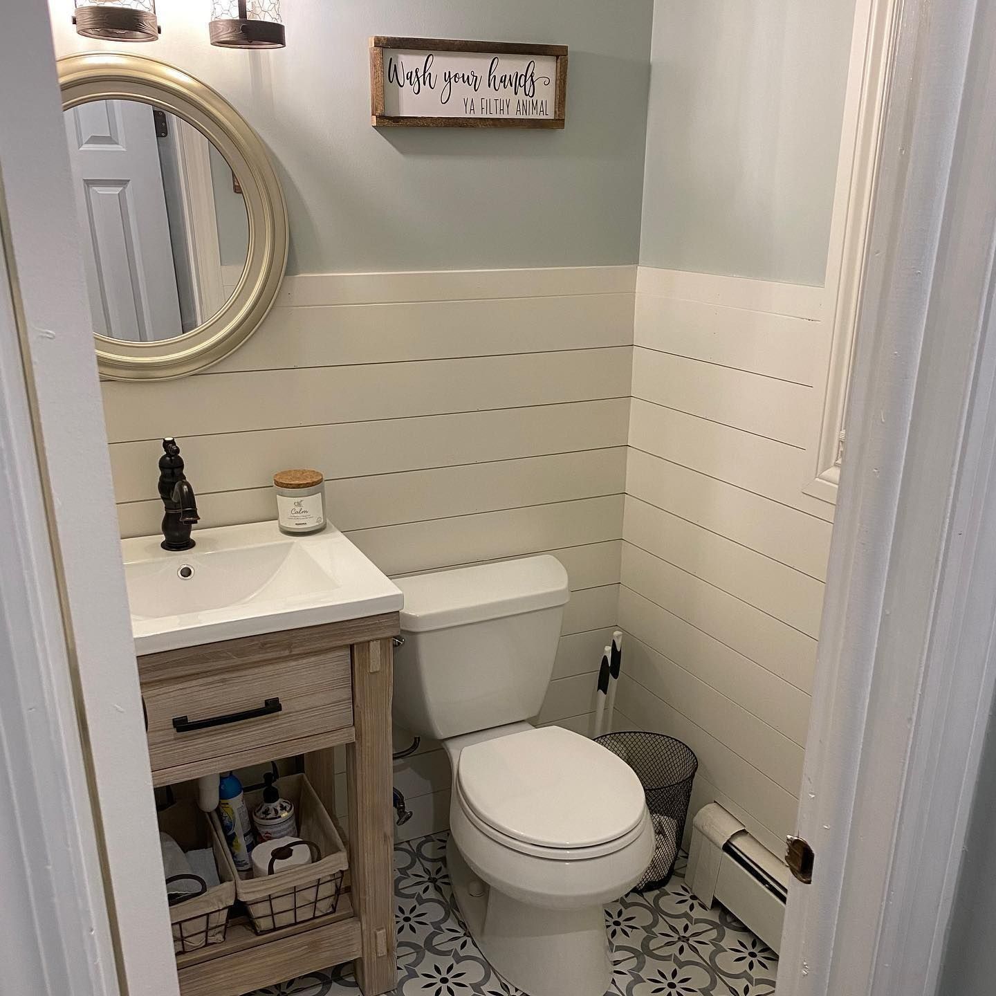 Small bathroom with a white toilet, sink, and shiplap walls. Gray and white patterned tile floor.