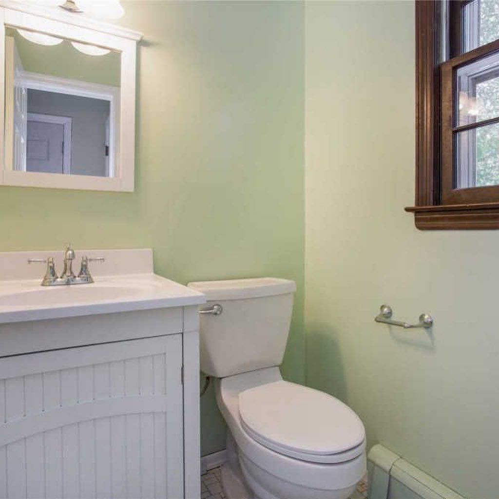 Bathroom with a white toilet, sink, and medicine cabinet; green walls and a brown-framed window.
