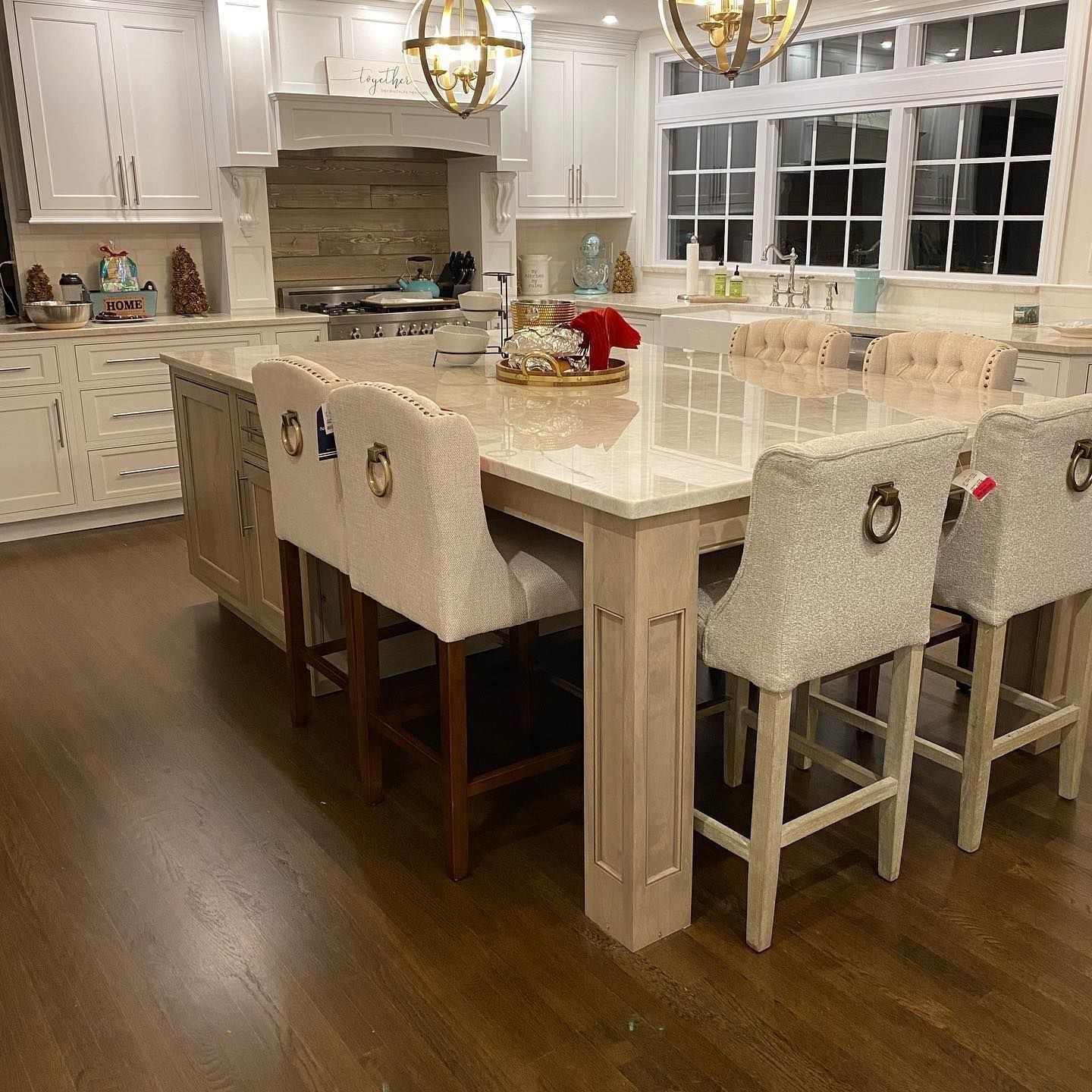 Kitchen with a large island, bar stools, white cabinets, and dark wood floors.