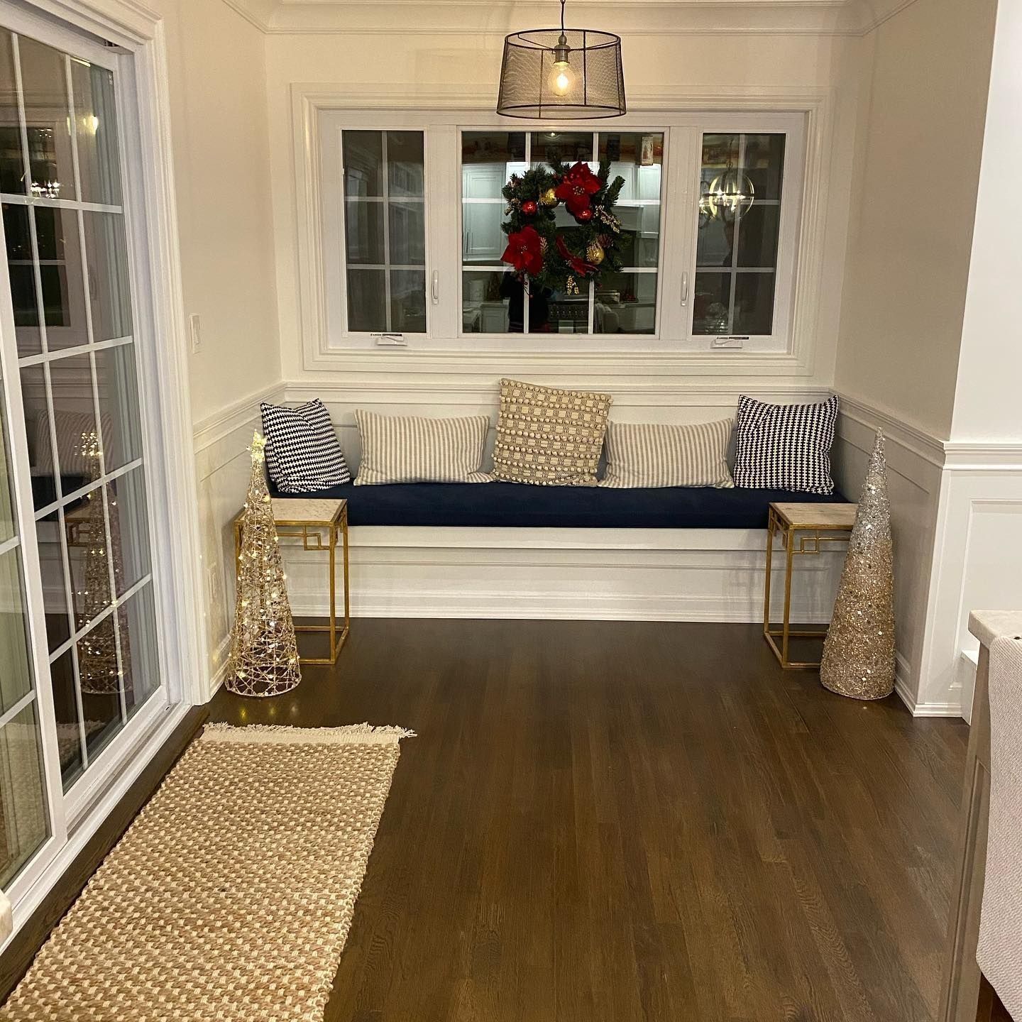 Sunroom with a window seat decorated for the holidays, lit with lamps and a rug.
