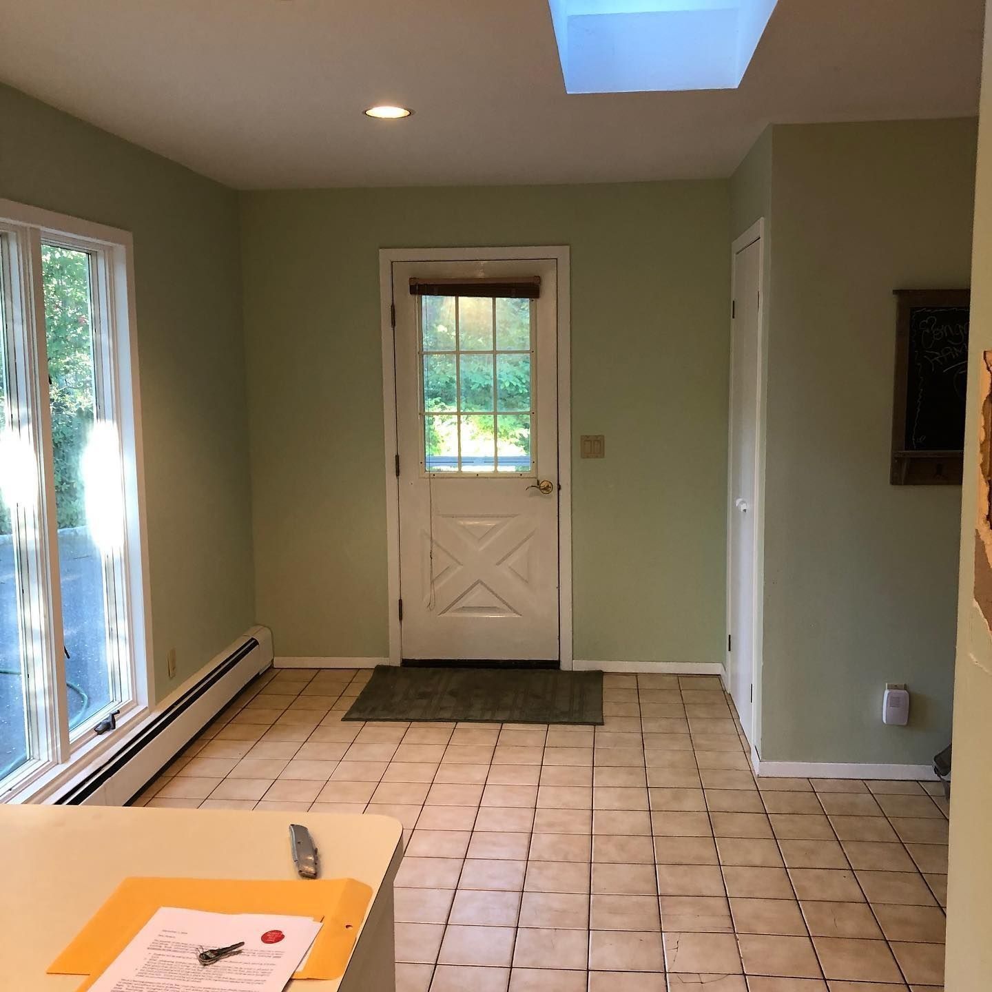 A room with green walls, tile floor, door, window, and skylight. A counter is in the foreground.