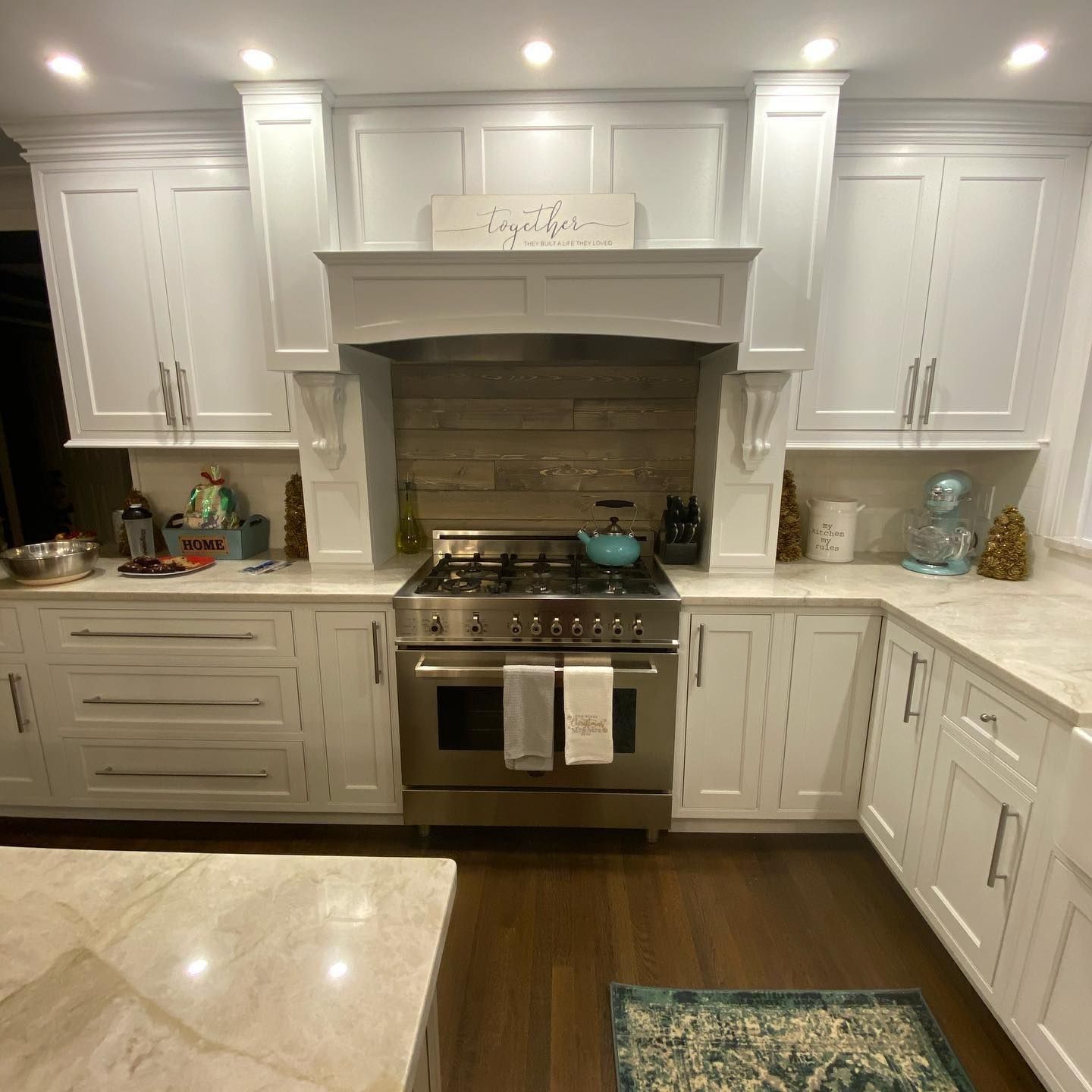 White kitchen with stainless steel range, light countertops, wood-look backsplash, and dark wood floor.