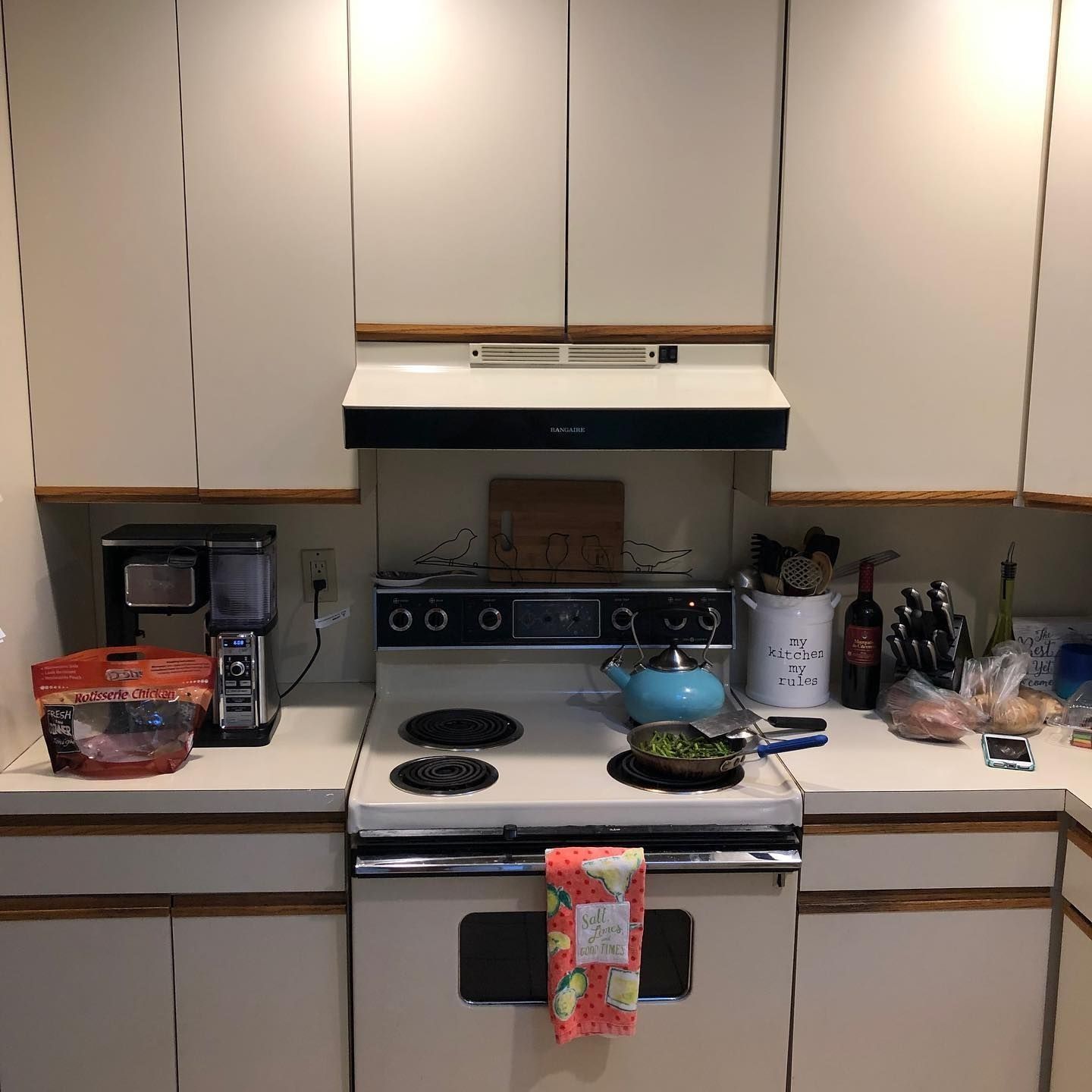 Kitchen with white cabinets, stove, coffee maker, and cooking supplies on countertops.