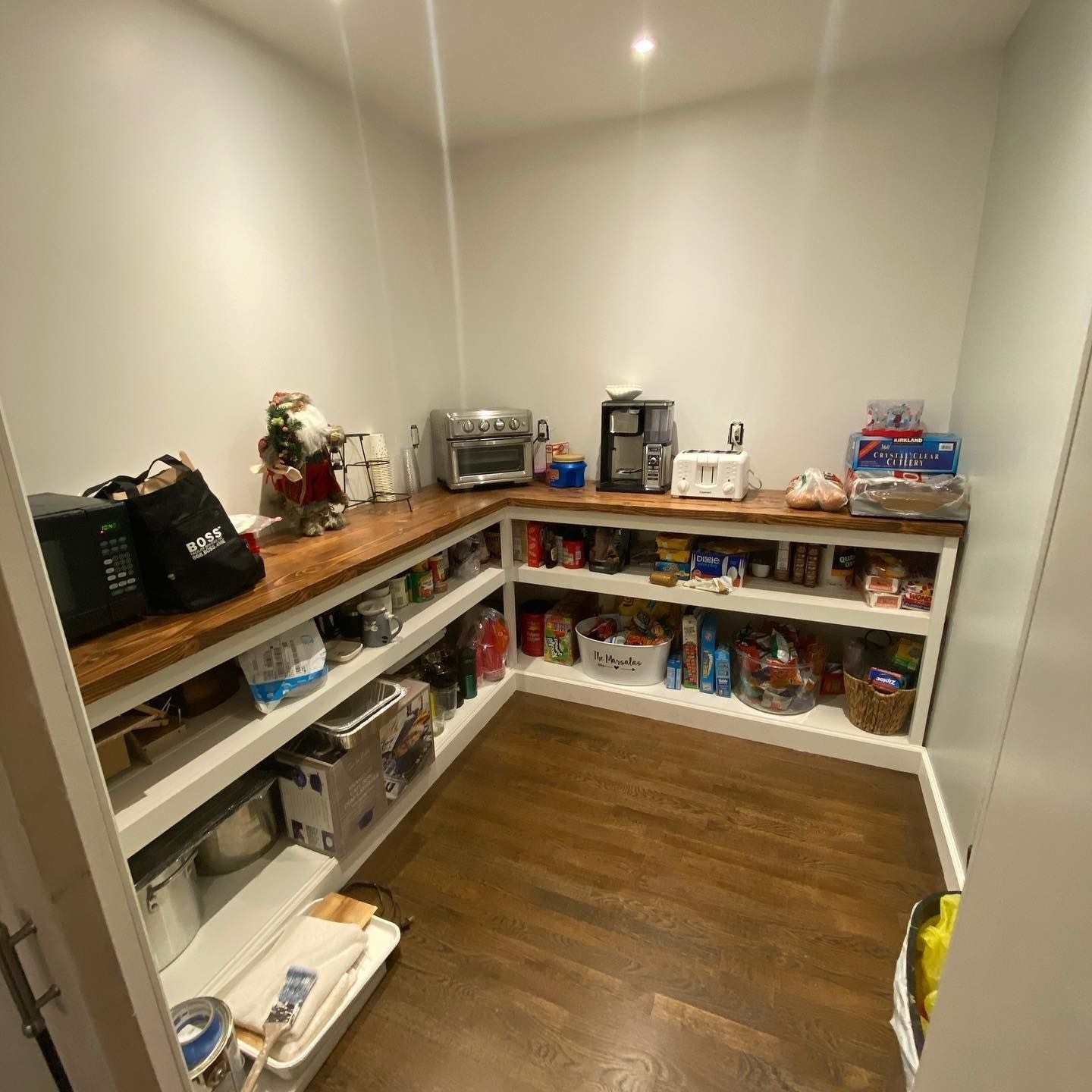 A well-stocked pantry with wooden countertops and white shelves filled with food items.