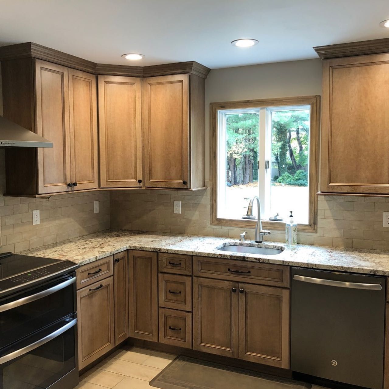 A kitchen with light wood cabinets, granite countertops, and a stainless steel sink and appliances.