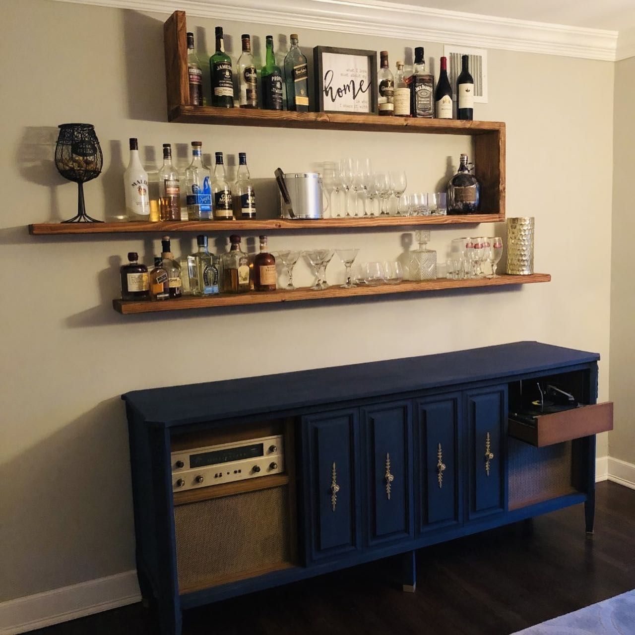 Bar area with blue cabinet, wooden shelves holding bottles and glasses.