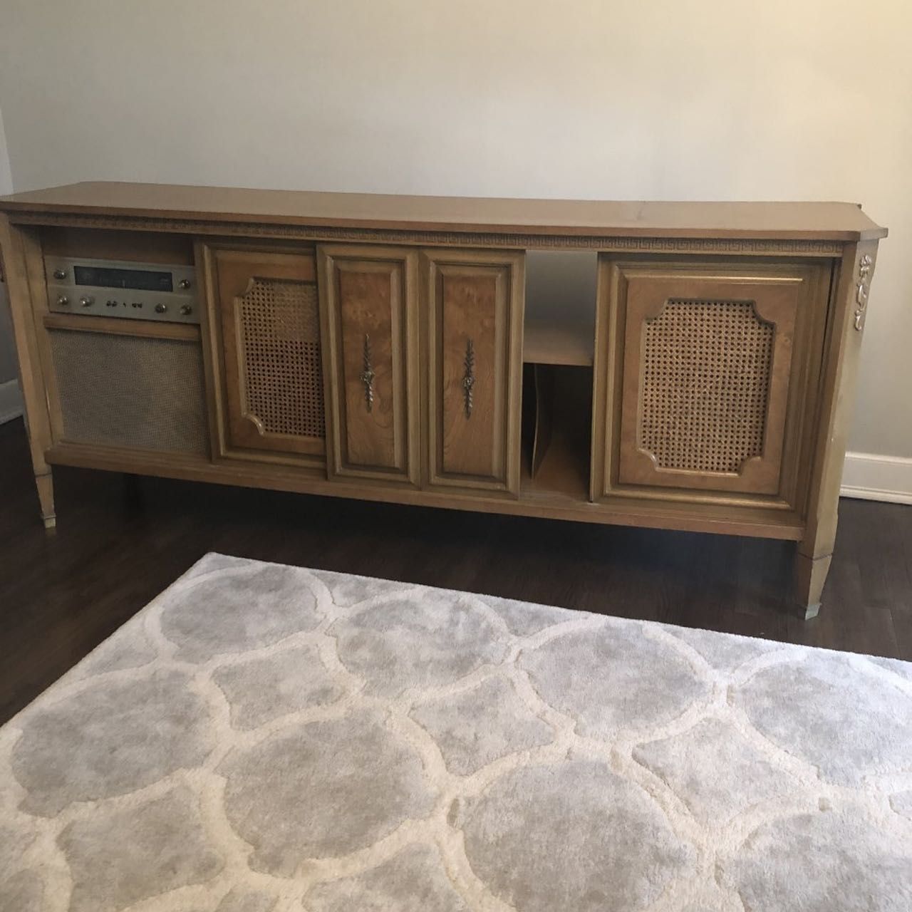 Tan mid-century modern stereo console cabinet with woven door panels and a light gray rug in front.