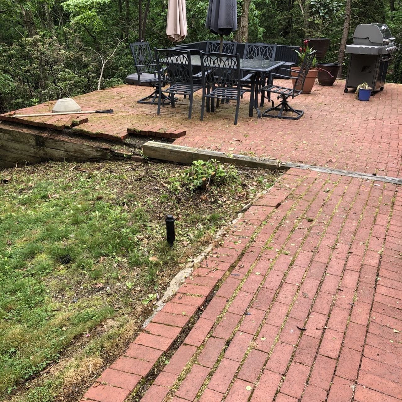 Brick patio with dining table and grill, steps down to grass and retaining wall.