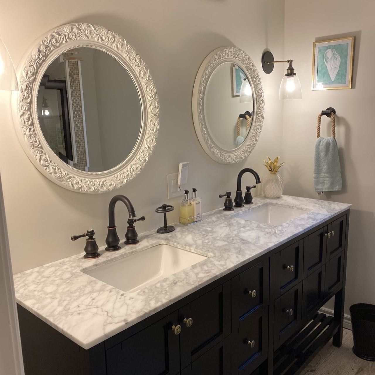 Bathroom vanity with black cabinets, marble countertop, and round framed mirrors.