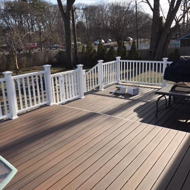 Wooden deck with white railing, and a black grill outside.