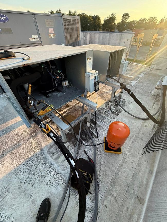 HVAC maintenance on a rooftop with refrigerant hoses connected to units and an orange recovery cylinder nearby.