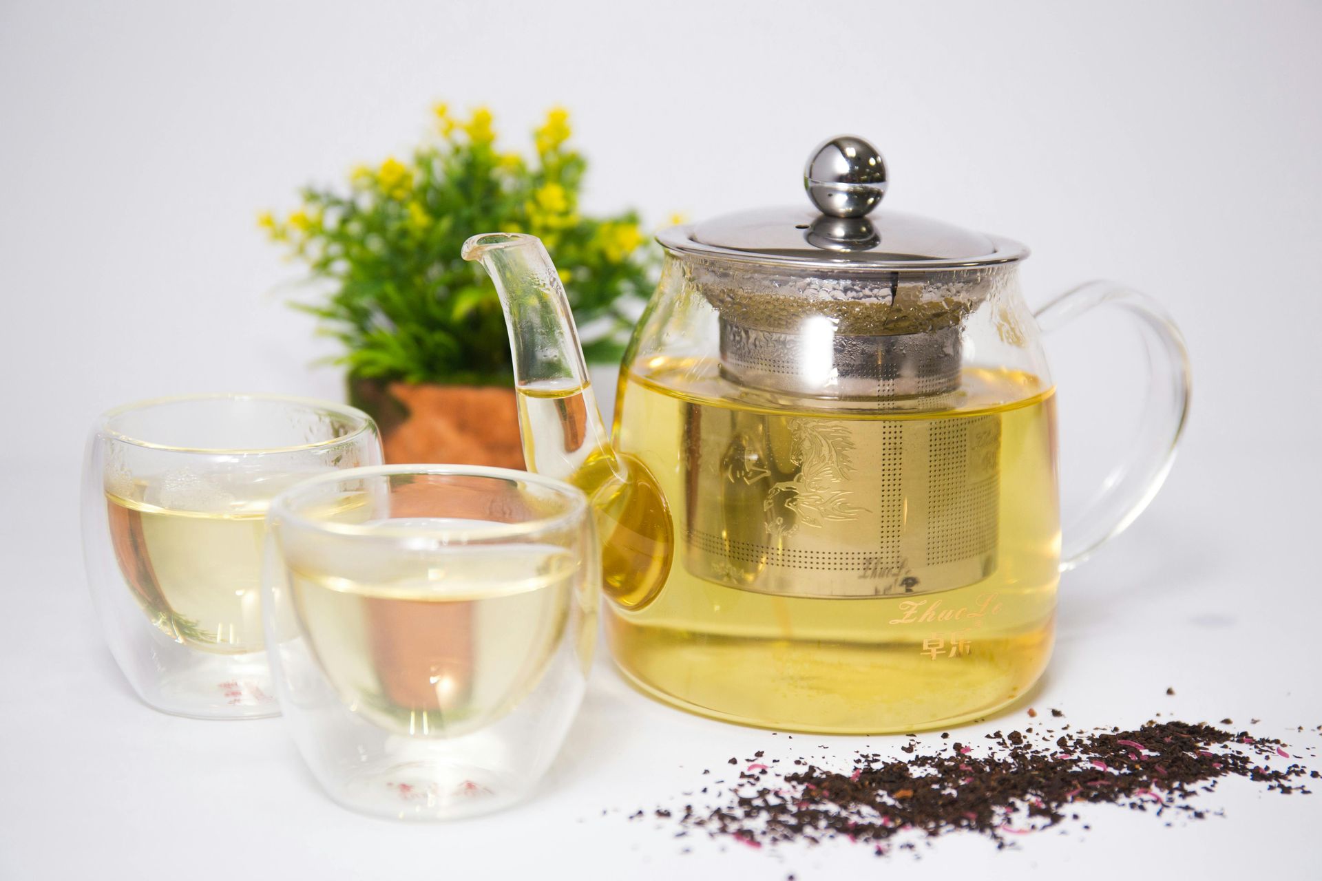 A glass teapot filled with tea next to two cups of tea.