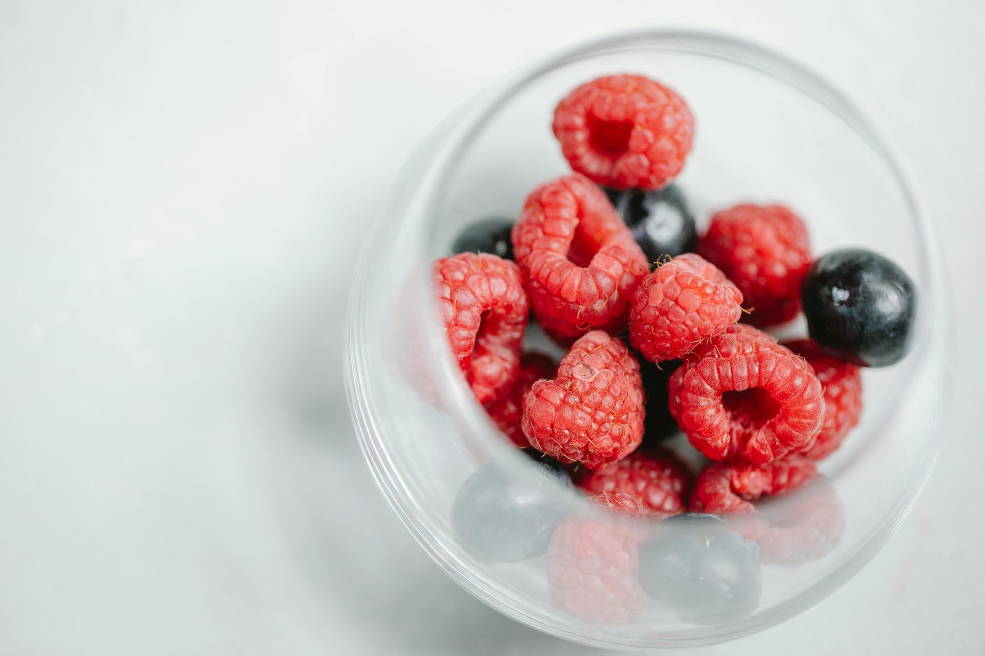 Raspberries and blueberries in a plastic bowl on a white surface.