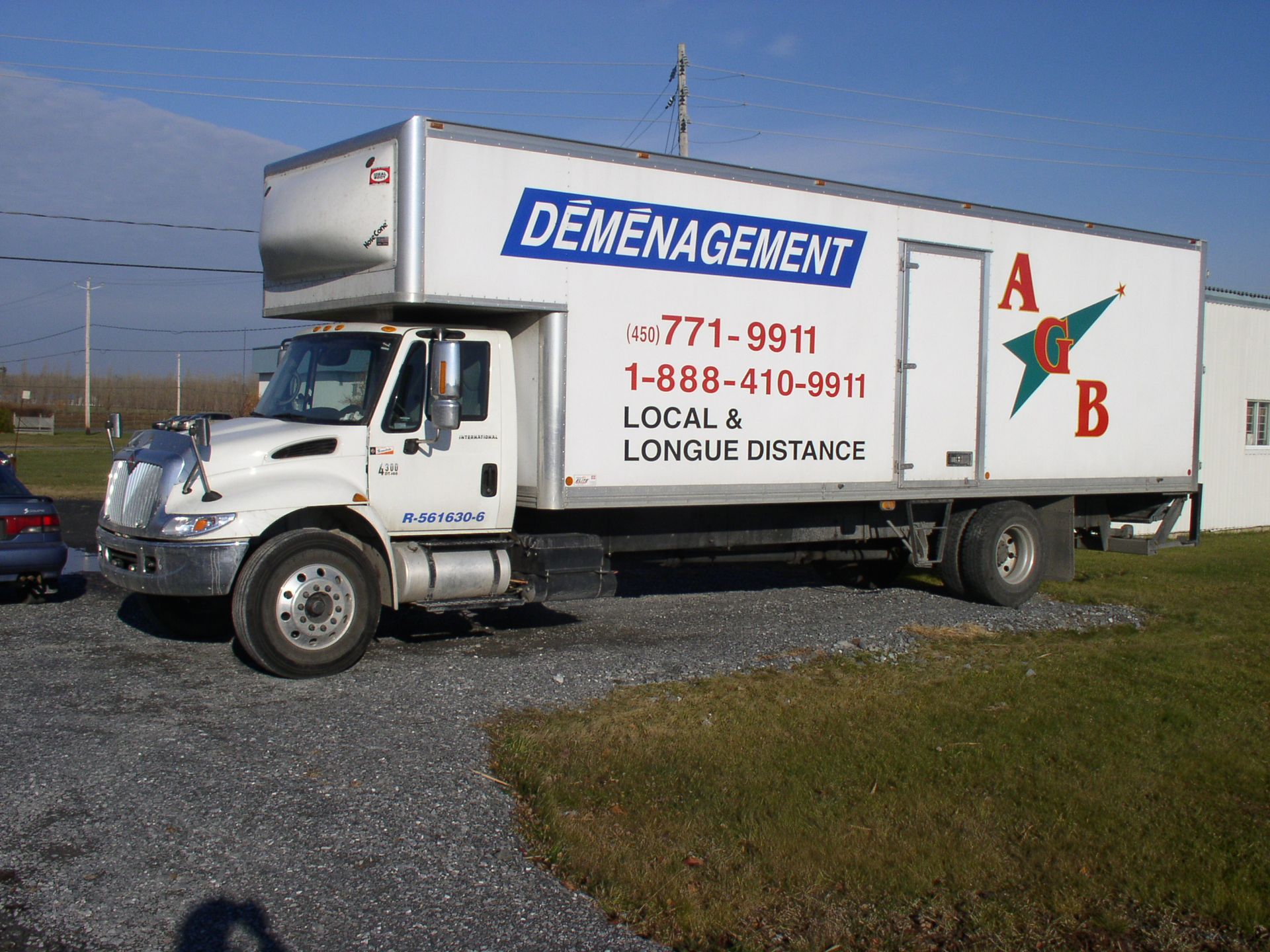 Camion de déménagement blanc avec logo bleu et rouge stationné sur du gravier et de l'herbe.