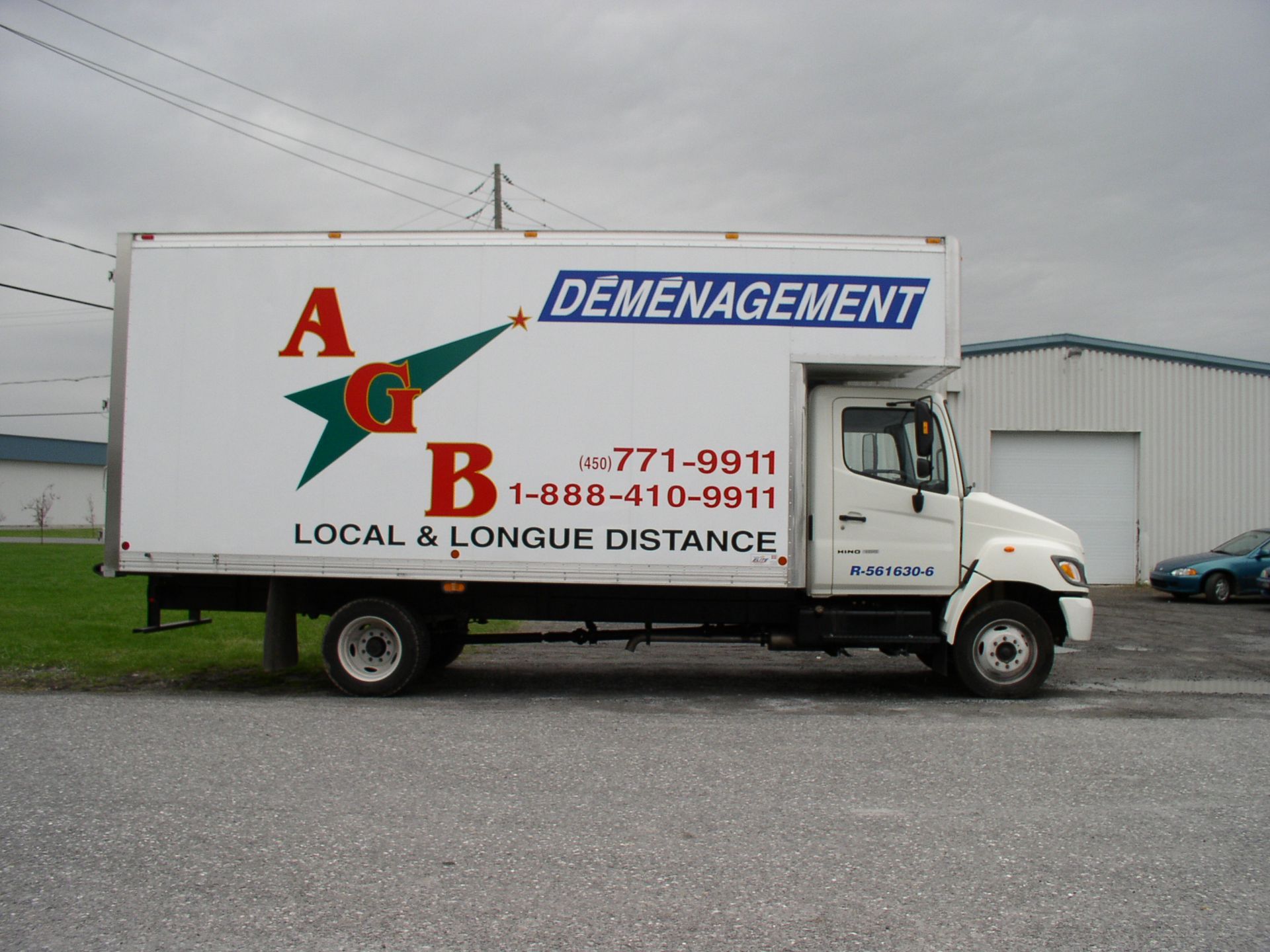 Un couple de personnes âgées déplace des cartons près d'un escalier. L'homme porte plusieurs cartons tandis que la femme n'en porte qu'un.