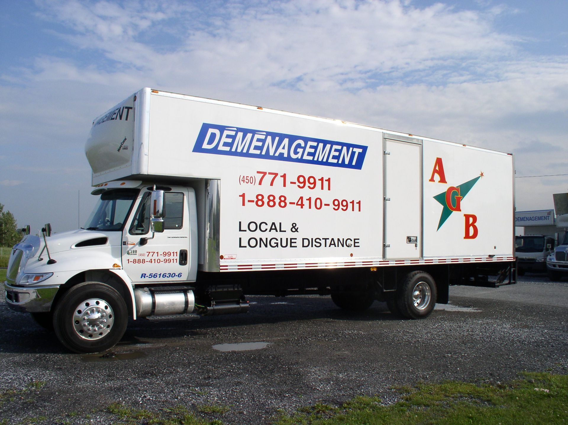 Camion de déménagement blanc avec logo bleu et vert, garé dehors sous un ciel bleu.