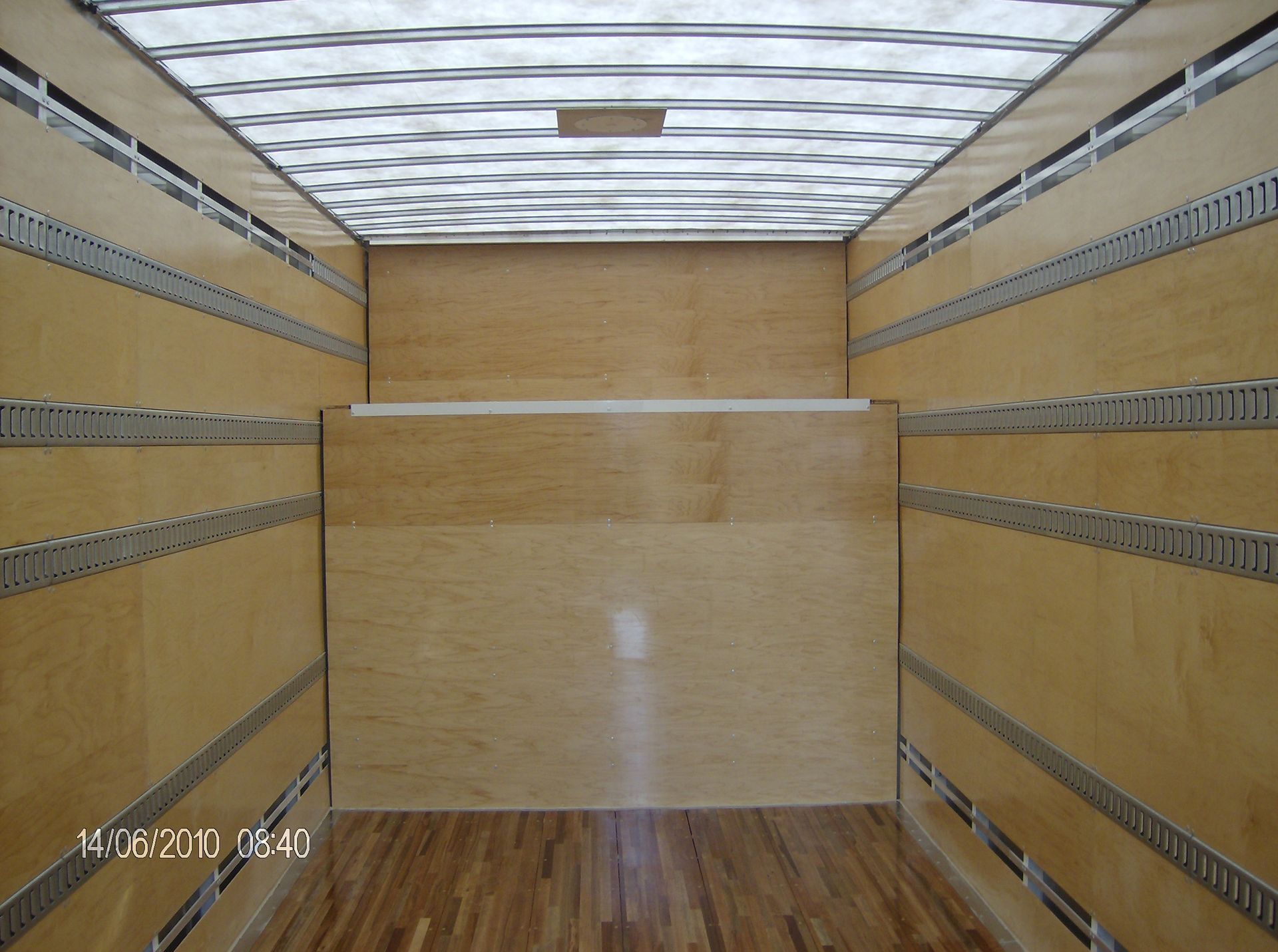 Intérieur de la zone de chargement d'un camion-caisse vide. Parois et plancher en contreplaqué, rails d'arrimage métalliques.