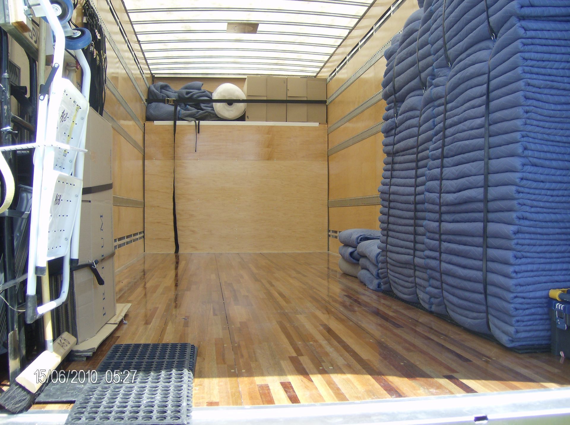À l'intérieur d'un camion de déménagement chargé de couvertures bleues pliées et d'autres objets. Sol et murs en bois.