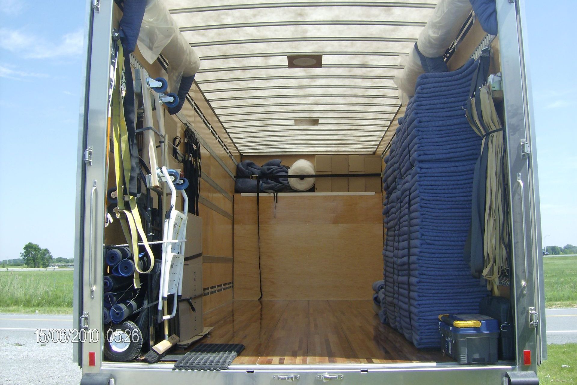 Intérieur d'une remorque, remplie d'équipement. Chaises bleues, caisse en bois et objets suspendus remplissent l'espace.