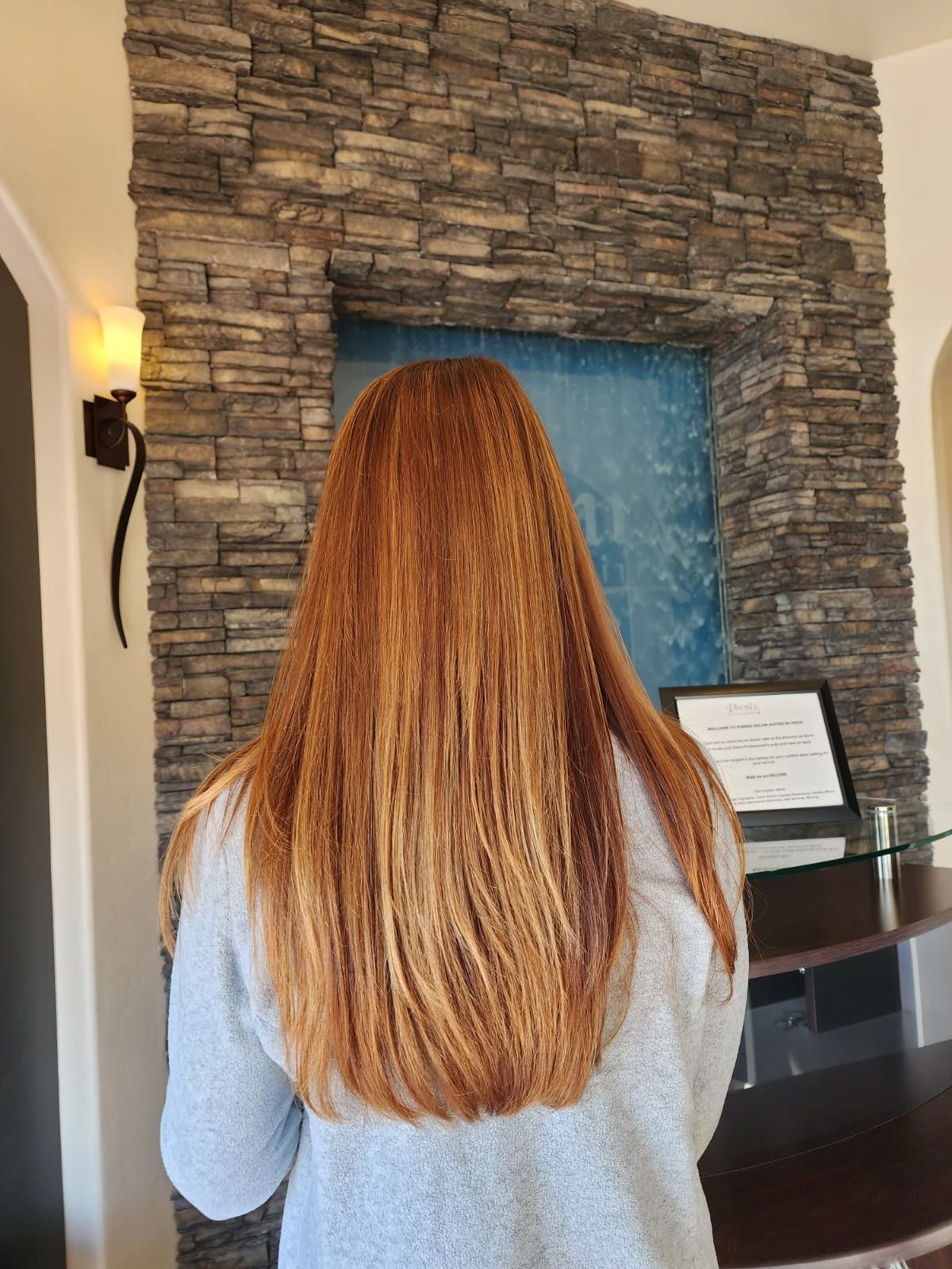 A woman with long red hair is standing in front of a stone wall.