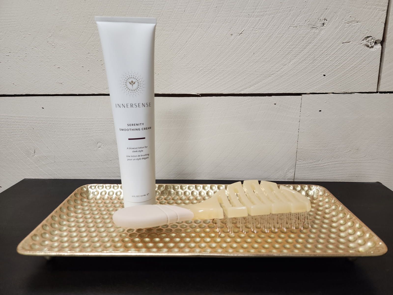 A gold tray with a tube of lotion and a brush on it