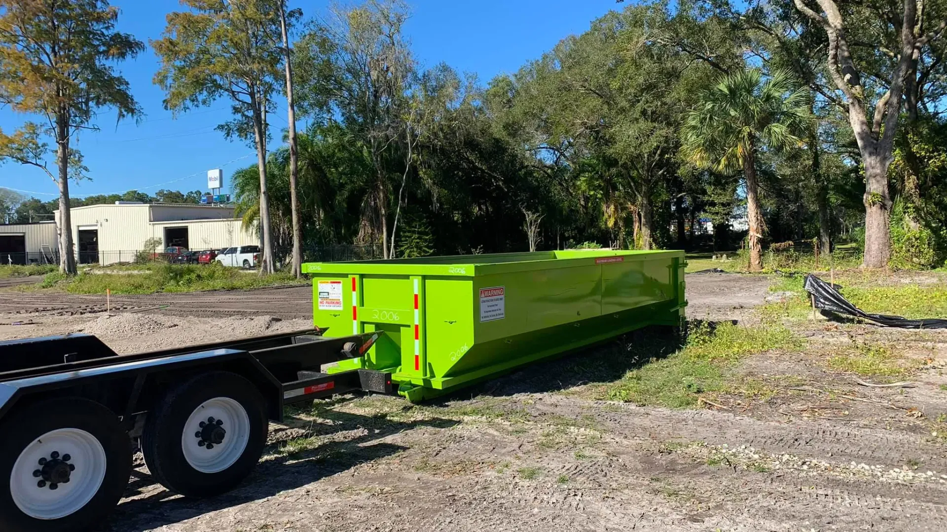 A green dumpster is sitting on top of a trailer in a gravel lot.