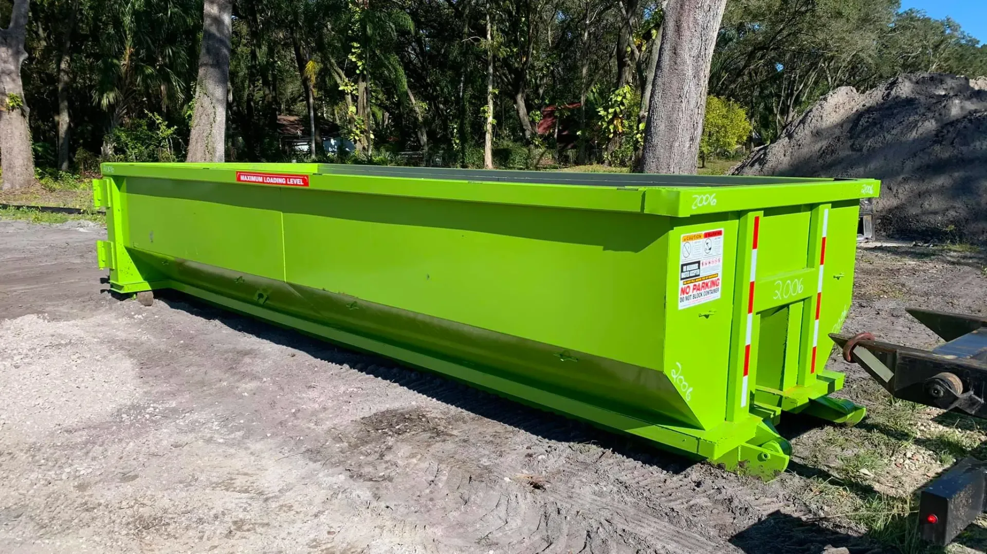 A green dumpster is sitting on top of a gravel road.
