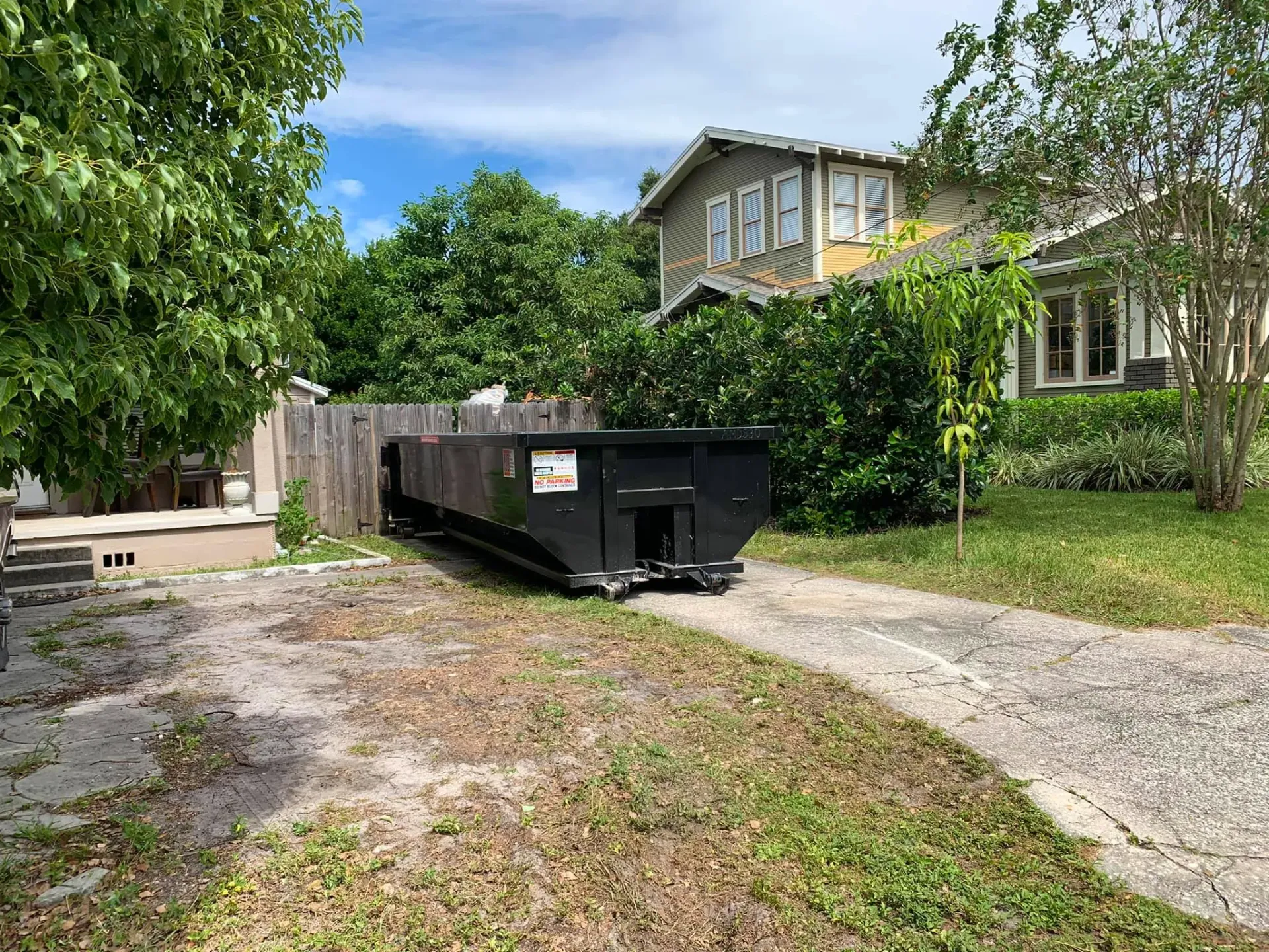 A dumpster is parked in the driveway of a house.