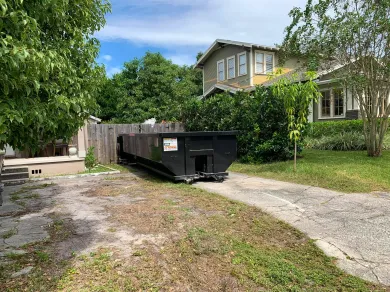A dumpster is parked in the driveway of a house.